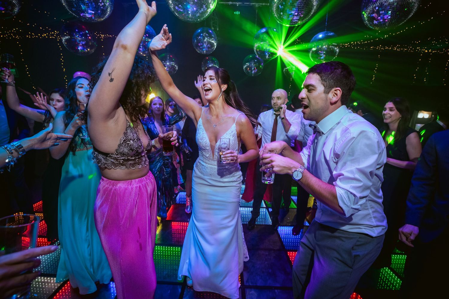 Bride and guests dancing joyfully on a colorful disco dance floor at a lively wedding reception party.