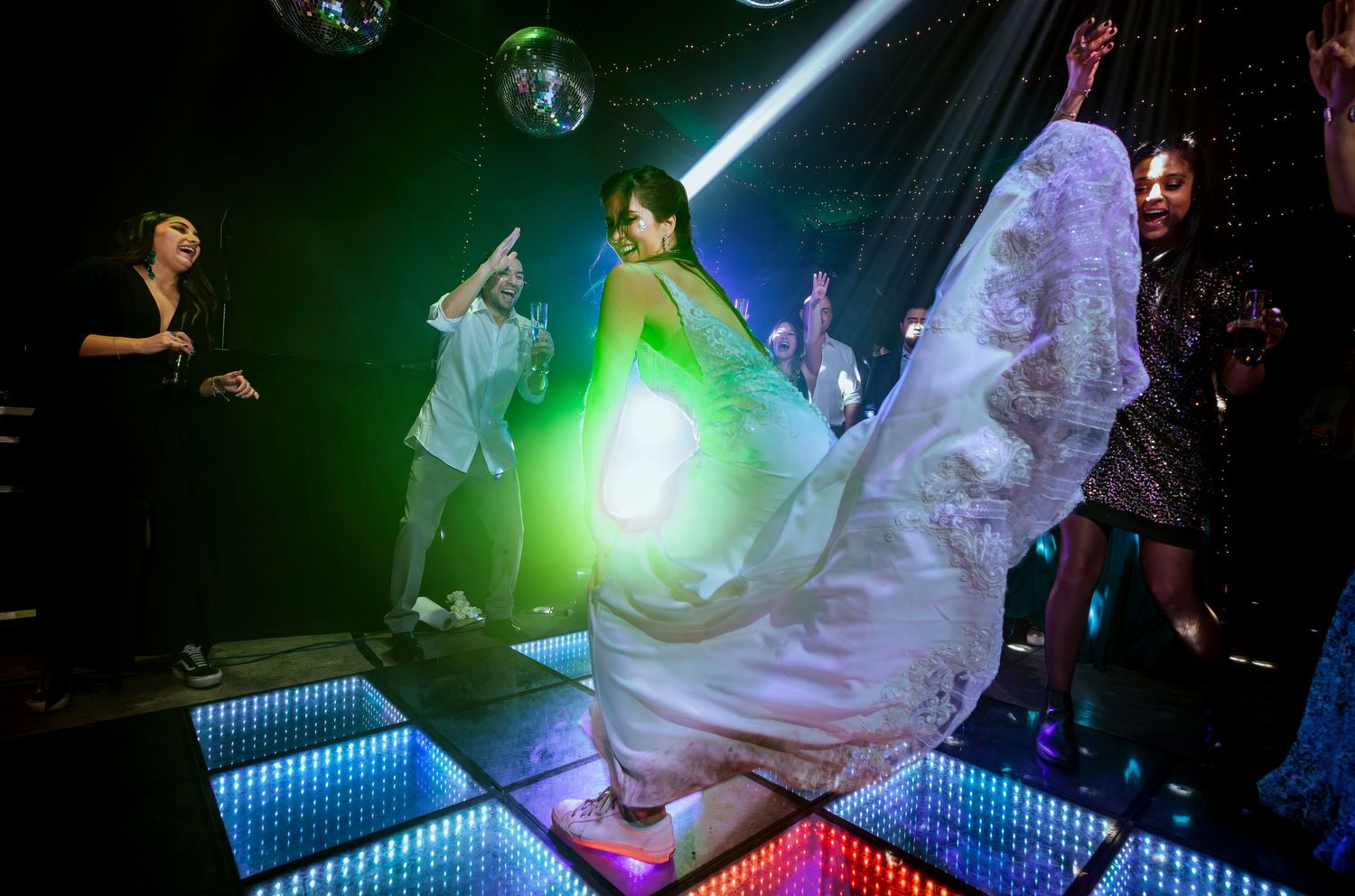 Bride dancing energetically on LED dance floor at nightclub wedding reception with guests celebrating around her.