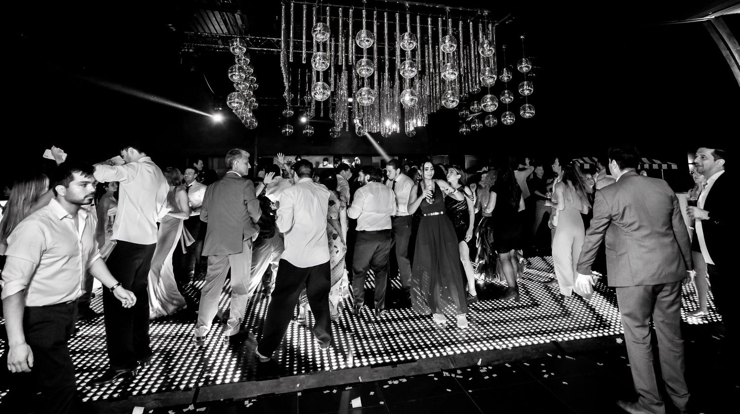 Wedding guests dancing on illuminated dance floor in black and white photo.