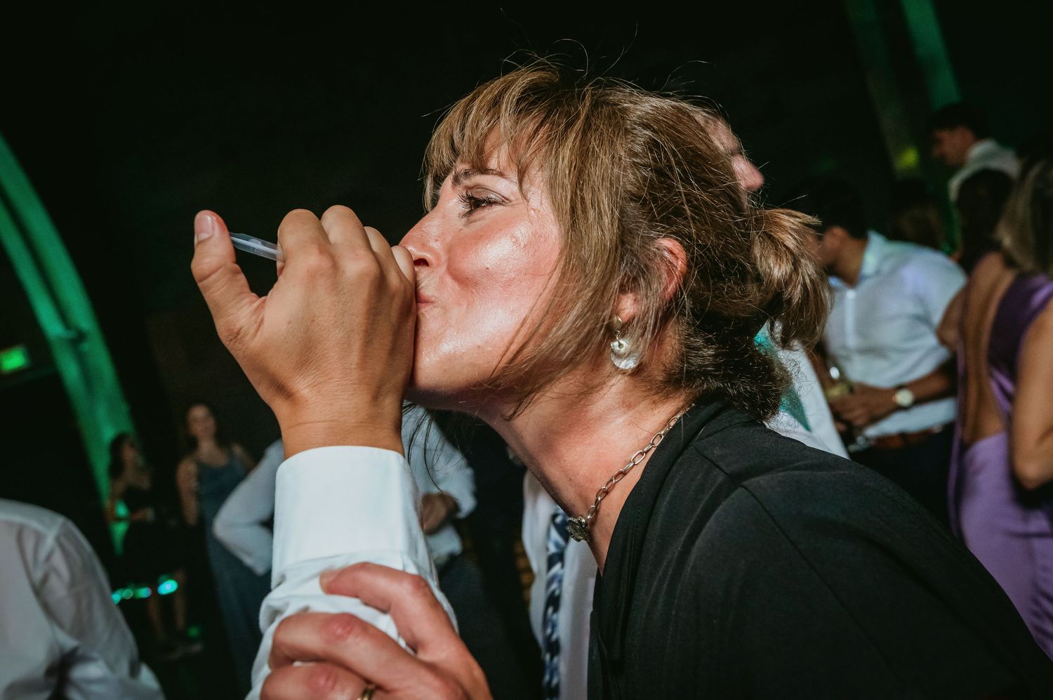 Woman drinks a shot from a syringe at a festive wedding reception party.