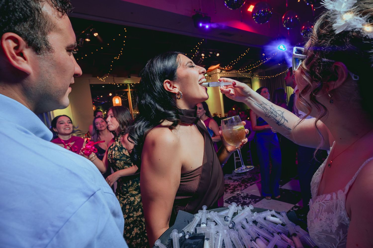 Woman laughing as bridesmaid pours shot at colorful wedding reception celebration.
