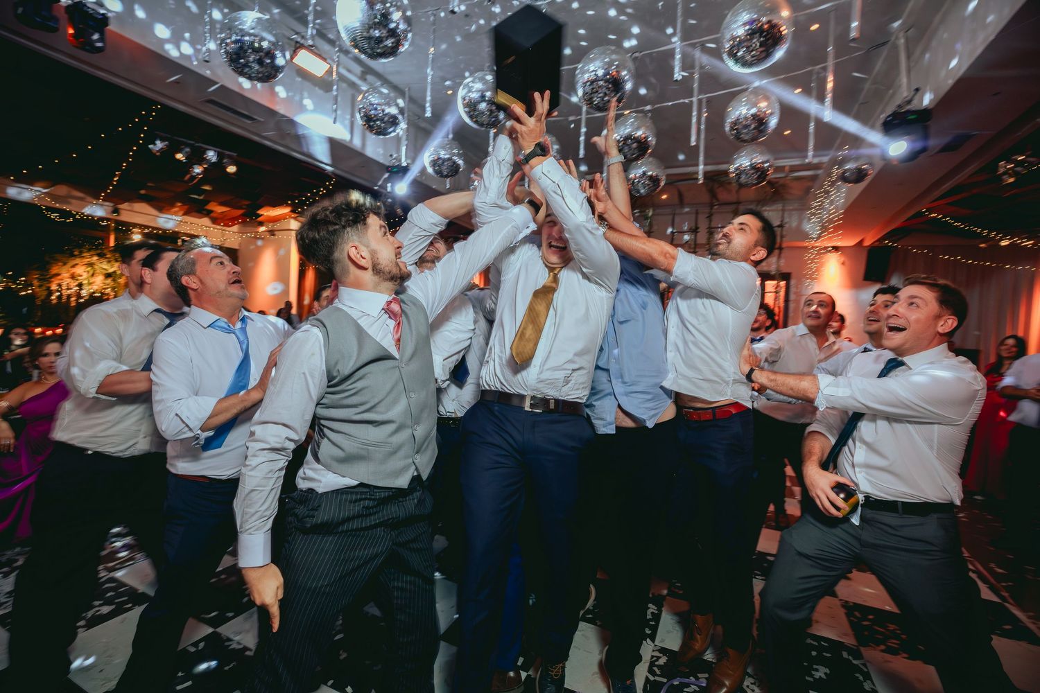 Groomsmen holding up trophy together under disco balls at festive wedding party.