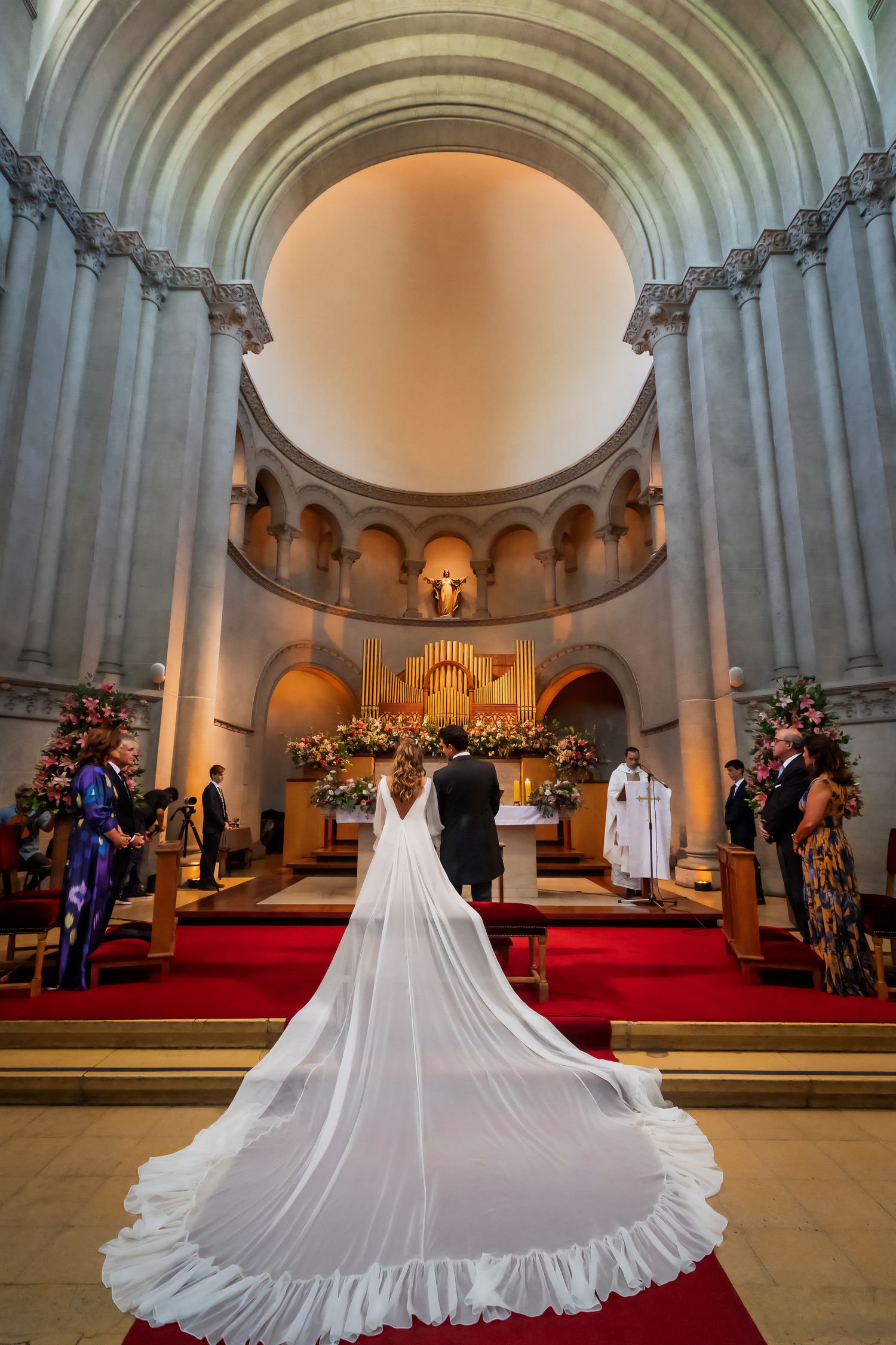 Bride in elegant gown with long cathedral veil walking toward altar in grand church.