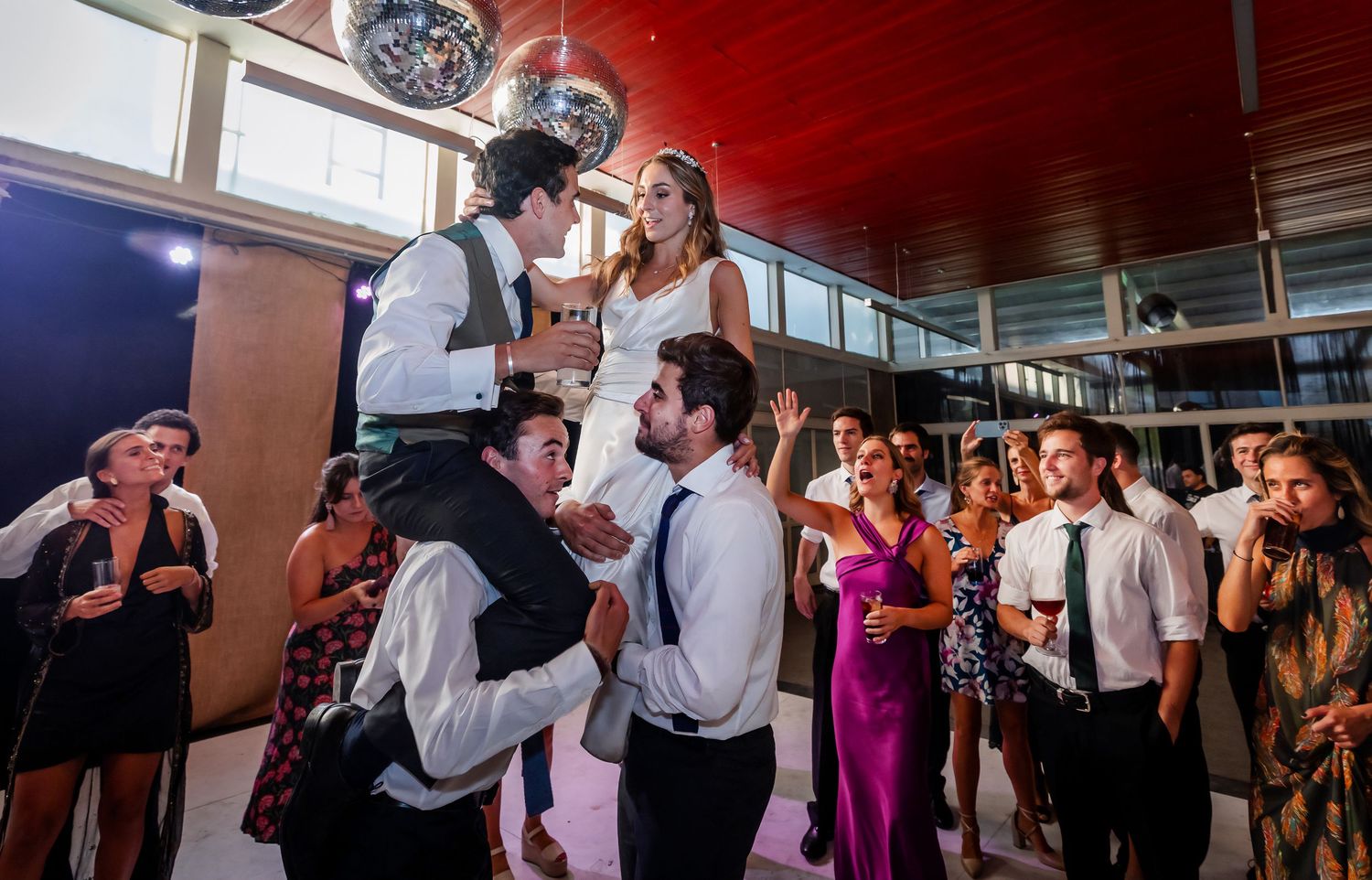 Bride and groom lifted on guests' shoulders celebrating joyfully at a festive wedding reception.
