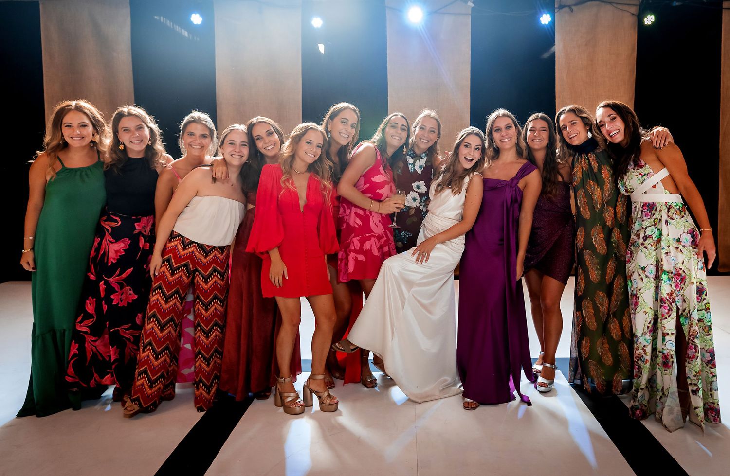 Group of women in colorful formal dresses pose together at a wedding celebration.