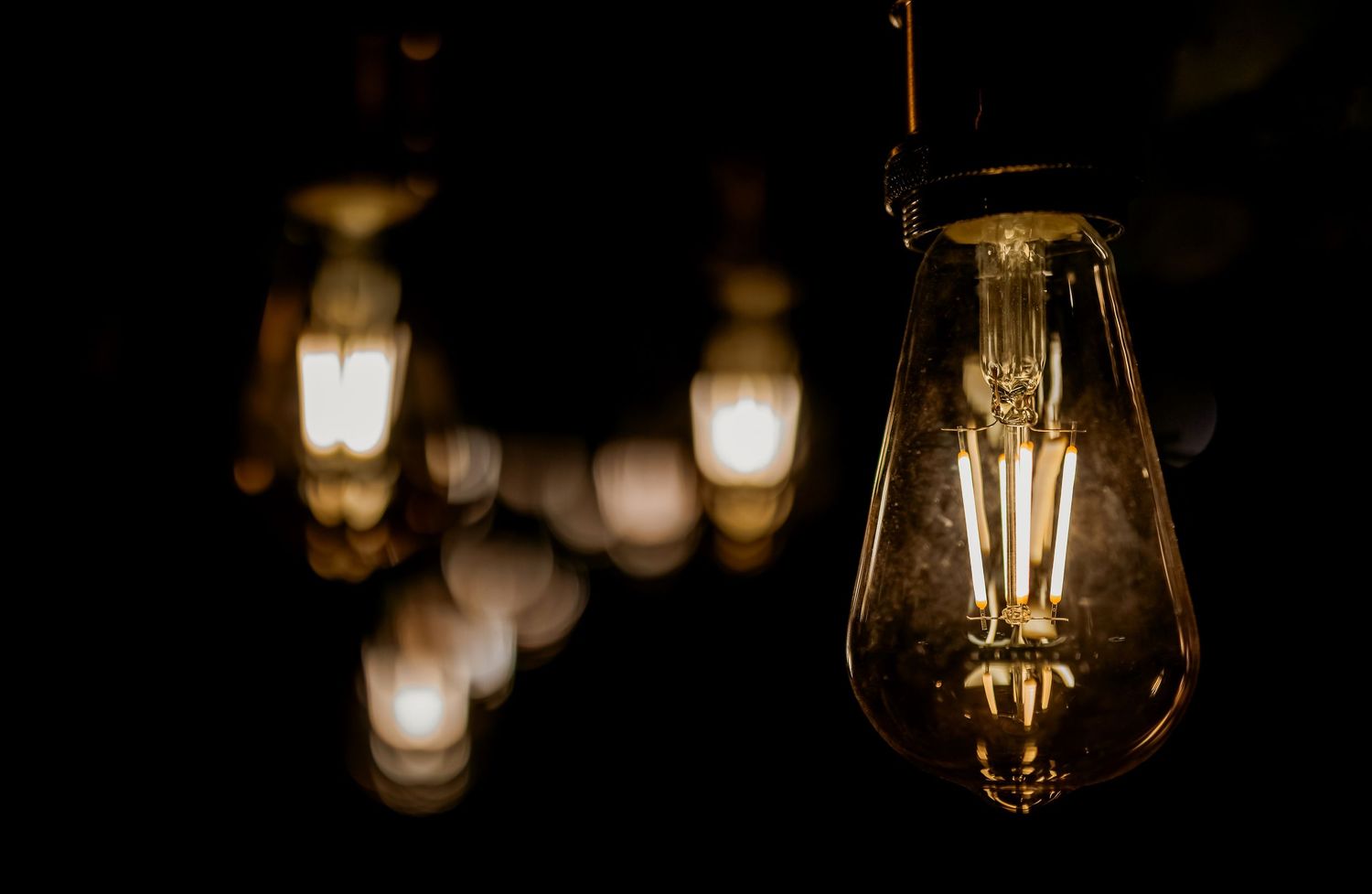 Vintage Edison bulbs glowing warmly in a dark room, showcasing filament details with bokeh light effects in the background.