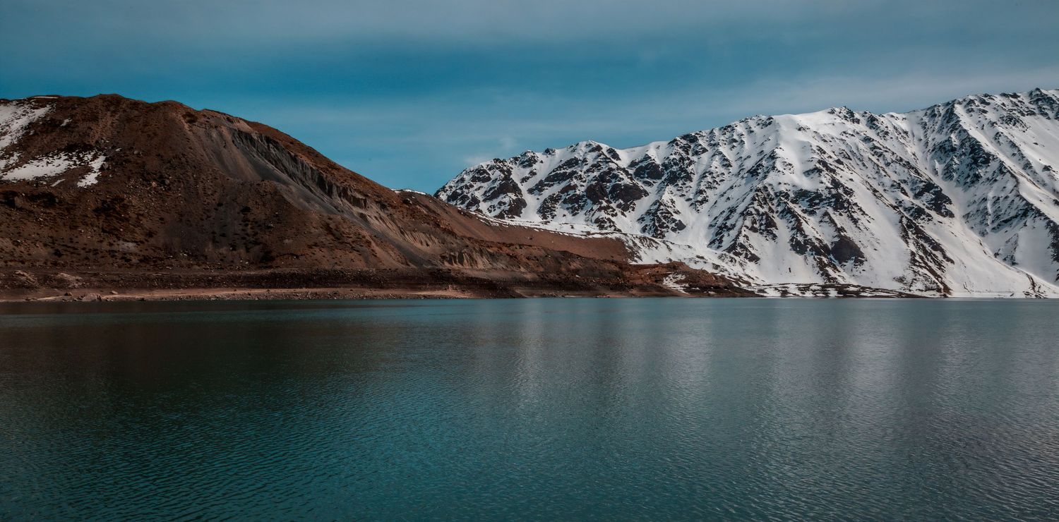Serene alpine lake reflecting snow-capped mountains under a blue sky in a stunning winter landscape.