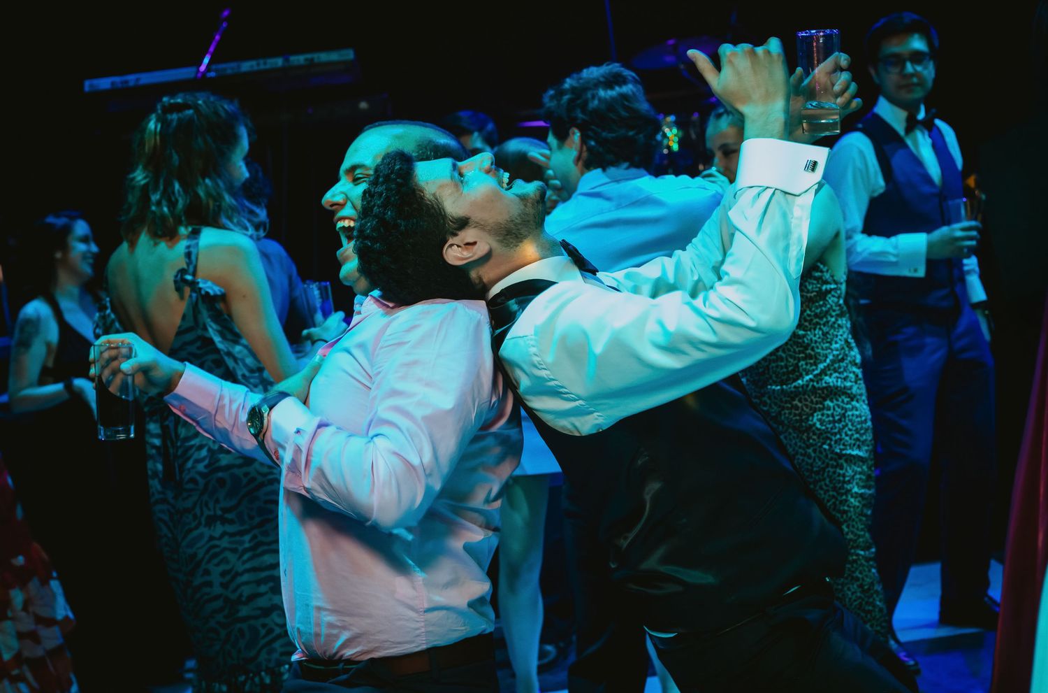 Two guests dance energetically together on a dimly lit wedding reception dance floor.