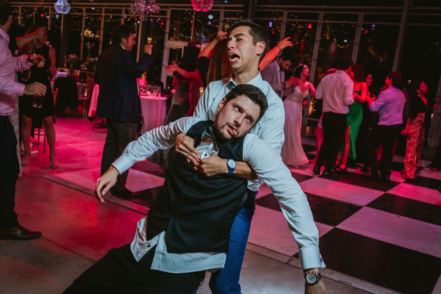 Two men playfully dancing and goofing around on a wedding reception dance floor.