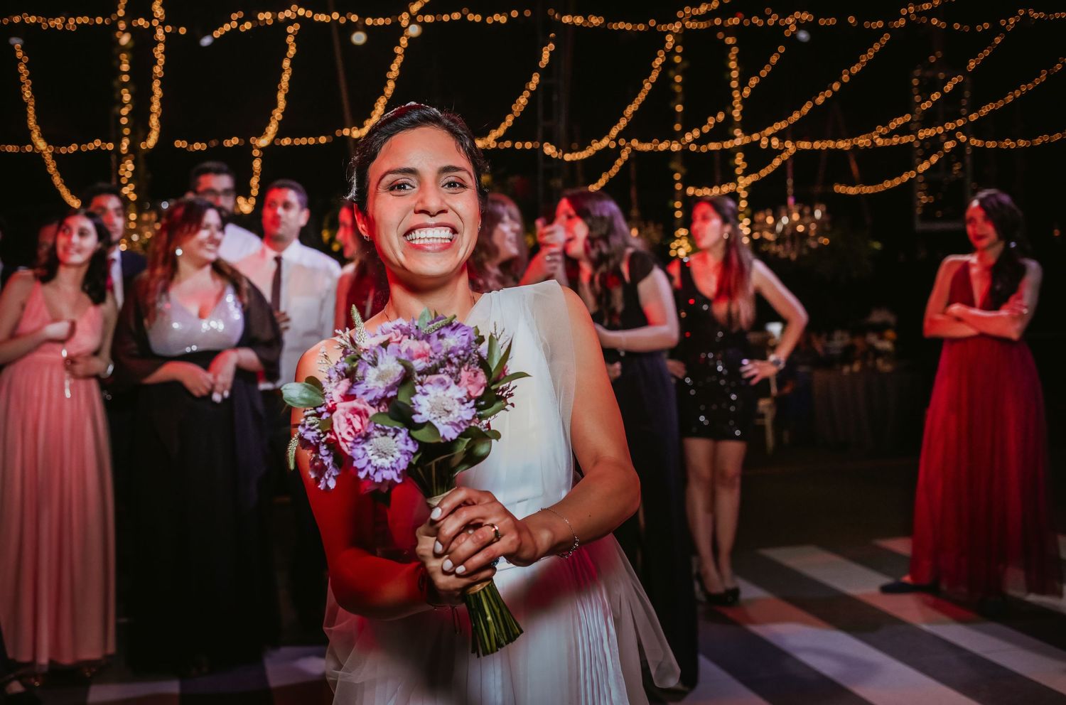 Happy bride holds purple floral bouquet after catching it at a wedding reception.