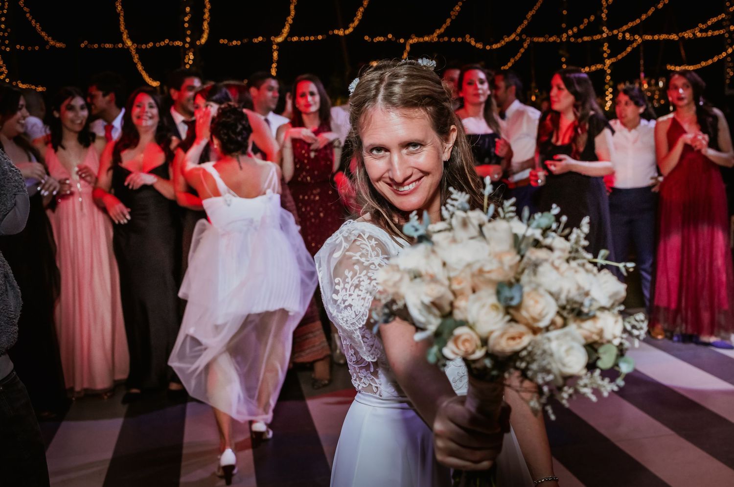 Bride in lace gown smiles holding white bouquet before toss at wedding reception.