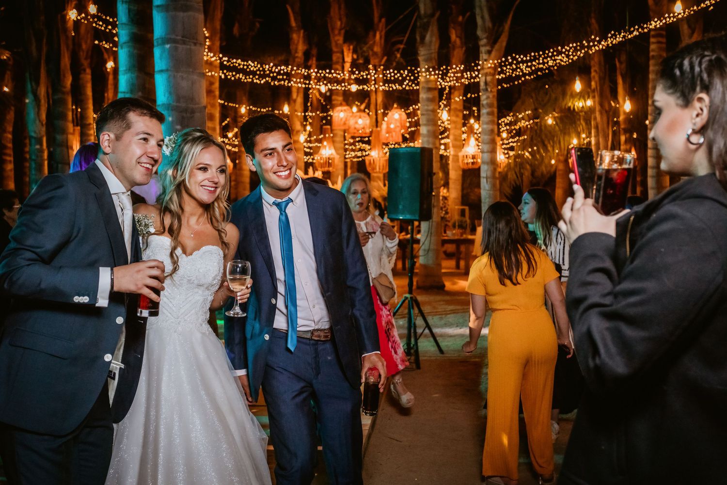 Bride in white gown mingles with guests on outdoor wedding dance floor under string lights.