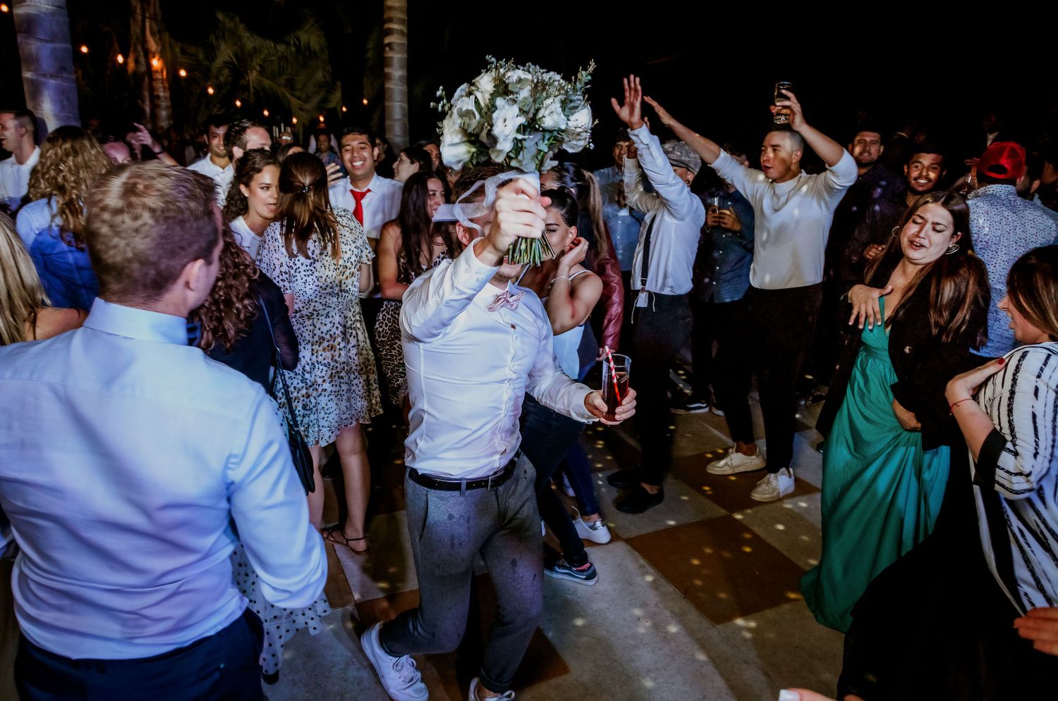 Wedding guest catches bouquet while crowd celebrates on outdoor dance floor at nighttime reception.