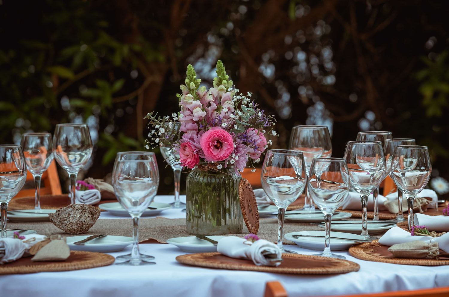 Elegant outdoor wedding table setting with pink floral centerpiece and crystal glassware.