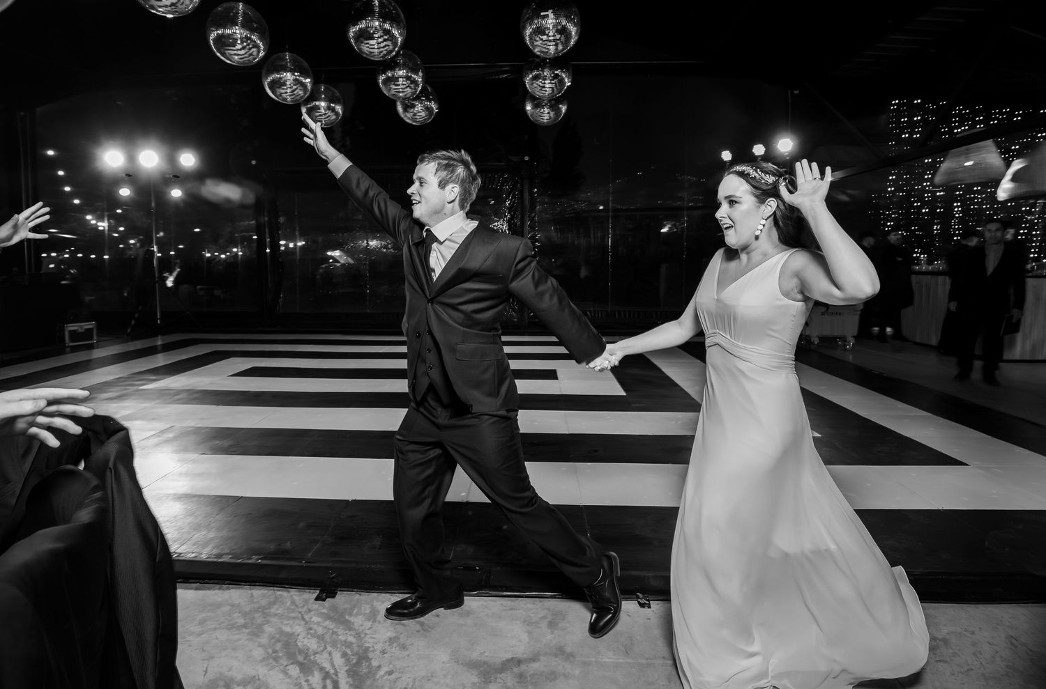 Black and white photo of couple dancing energetically on checkered wedding dance floor.