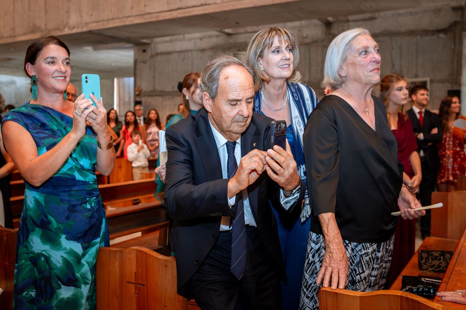 Guests smile and take photos on smartphones during a church wedding ceremony.