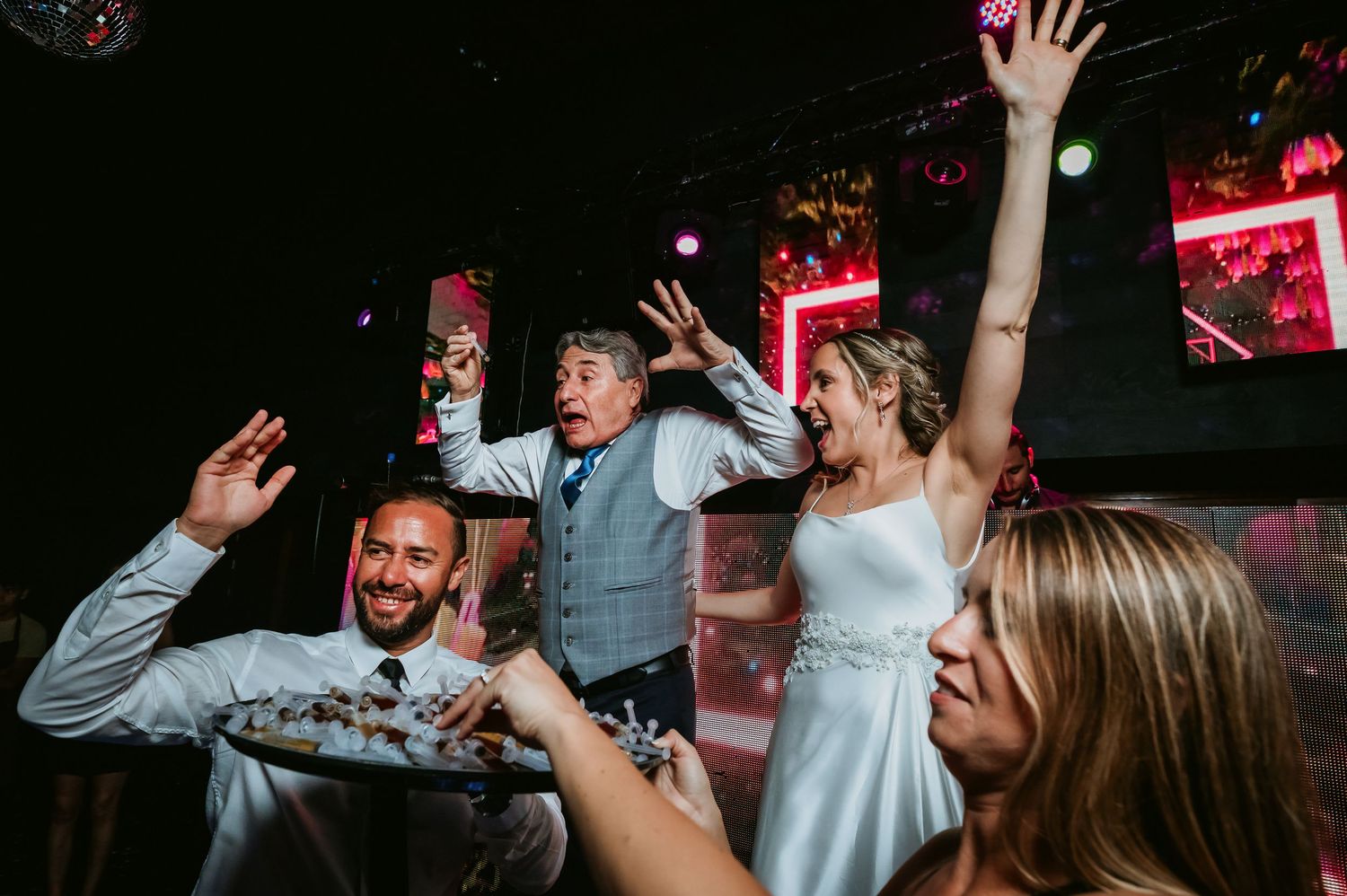 Bride and guests celebrate joyfully with raised hands at a vibrant wedding reception.