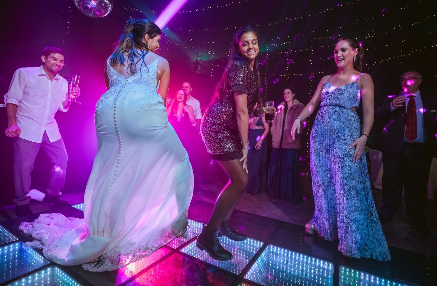 Women dancing at a glamorous party on a lit dance floor under disco lights.