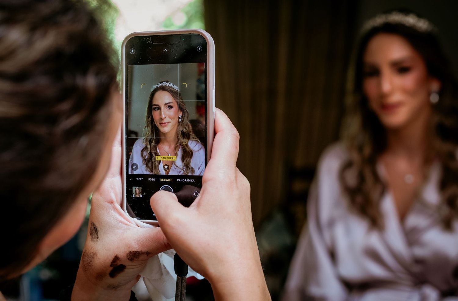 Someone photographs a bride wearing a tiara with a smartphone camera during wedding preparations.