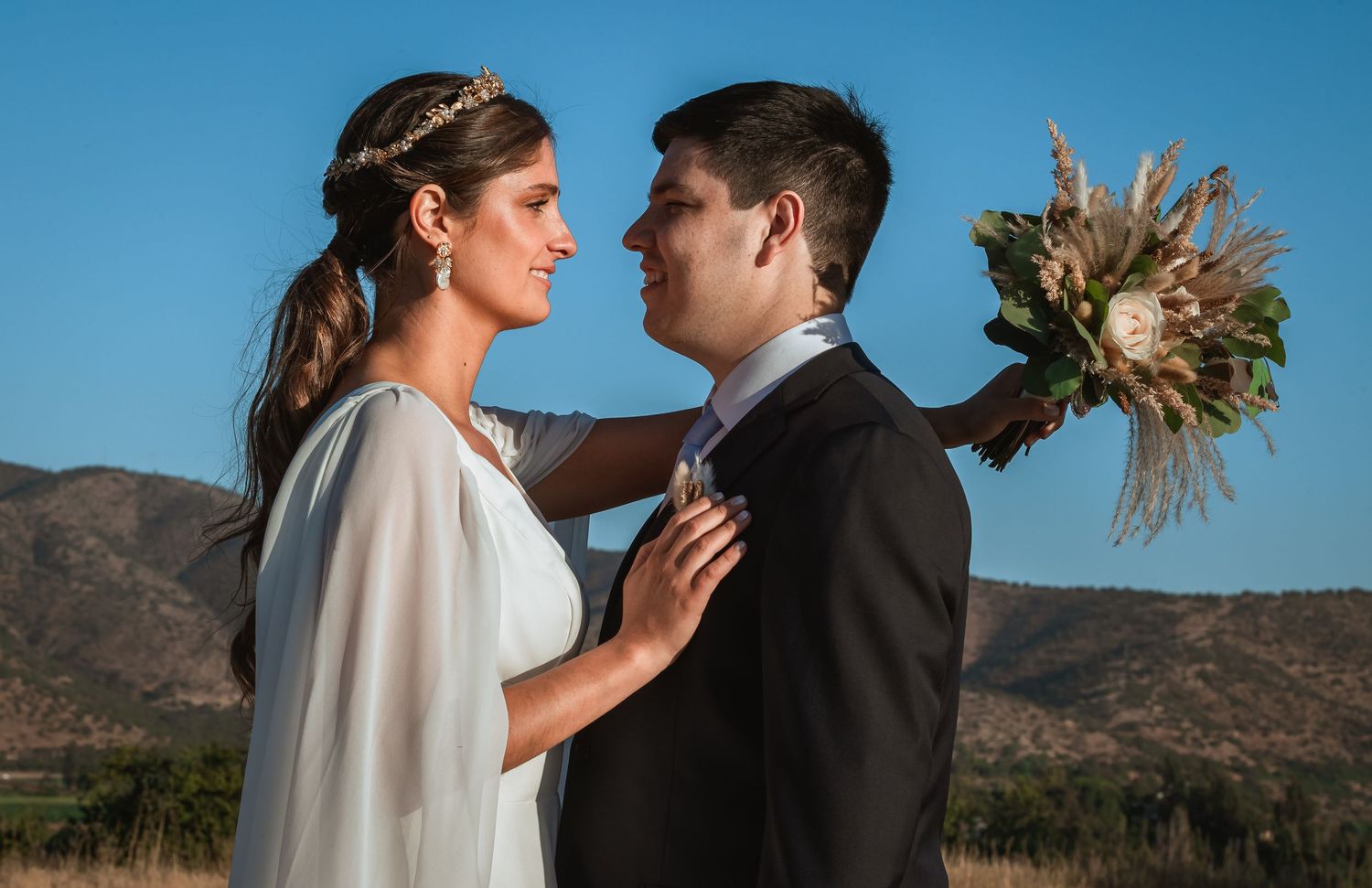 Bride and groom share a tender moment gazing at each other with mountain backdrop and bouquet.