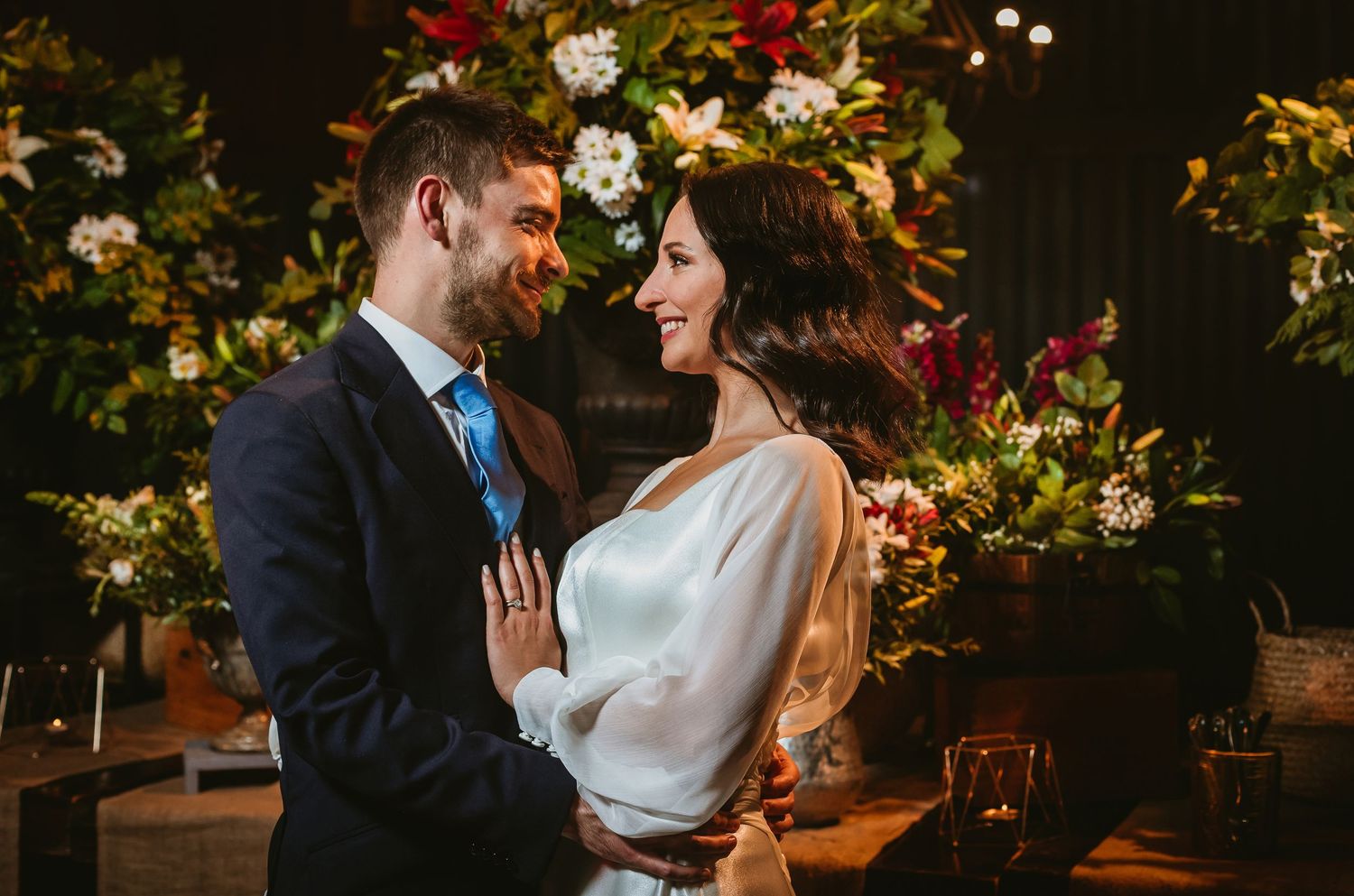 Bride and groom share a romantic moment surrounded by lush floral arrangements at their wedding ceremony.