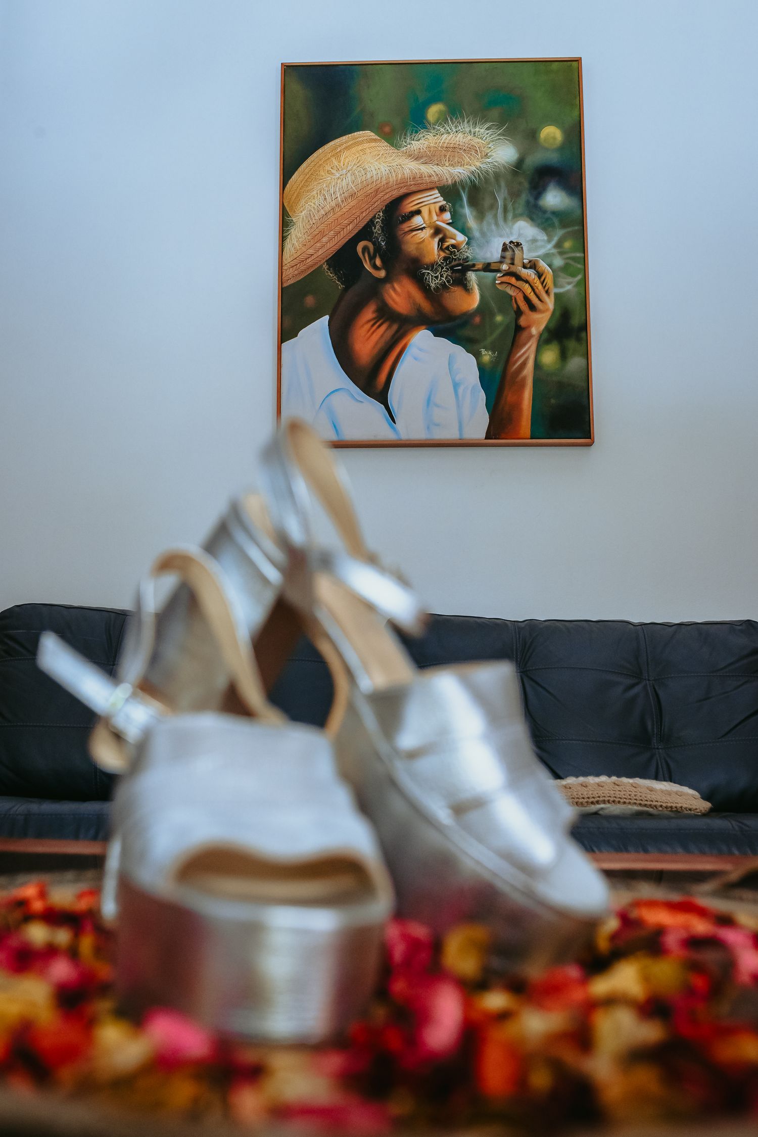 Silver bridal heels displayed on a table with a colorful painting of a man in a hat behind.