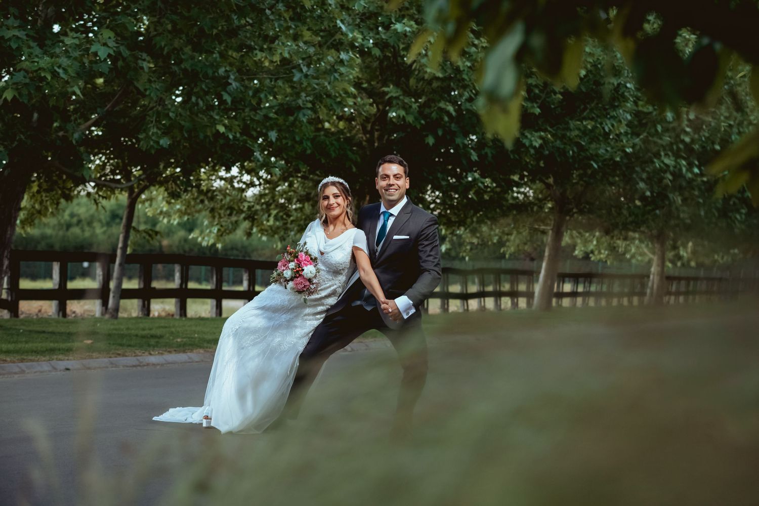 Joyful bride and groom laughing and running together through a lush green garden on their wedding day.