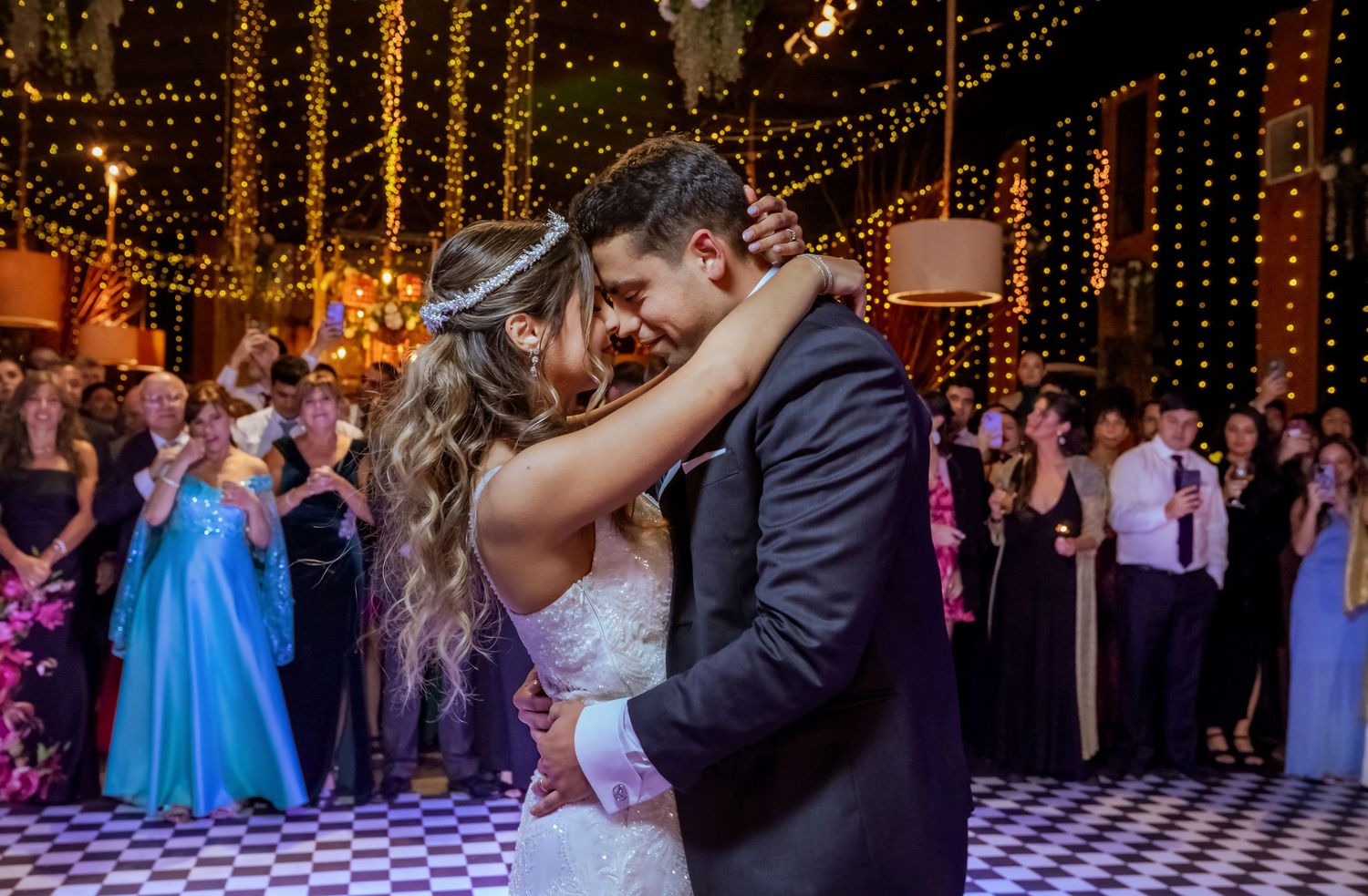 Bride and groom share their first dance in a warmly lit wedding venue with string lights.