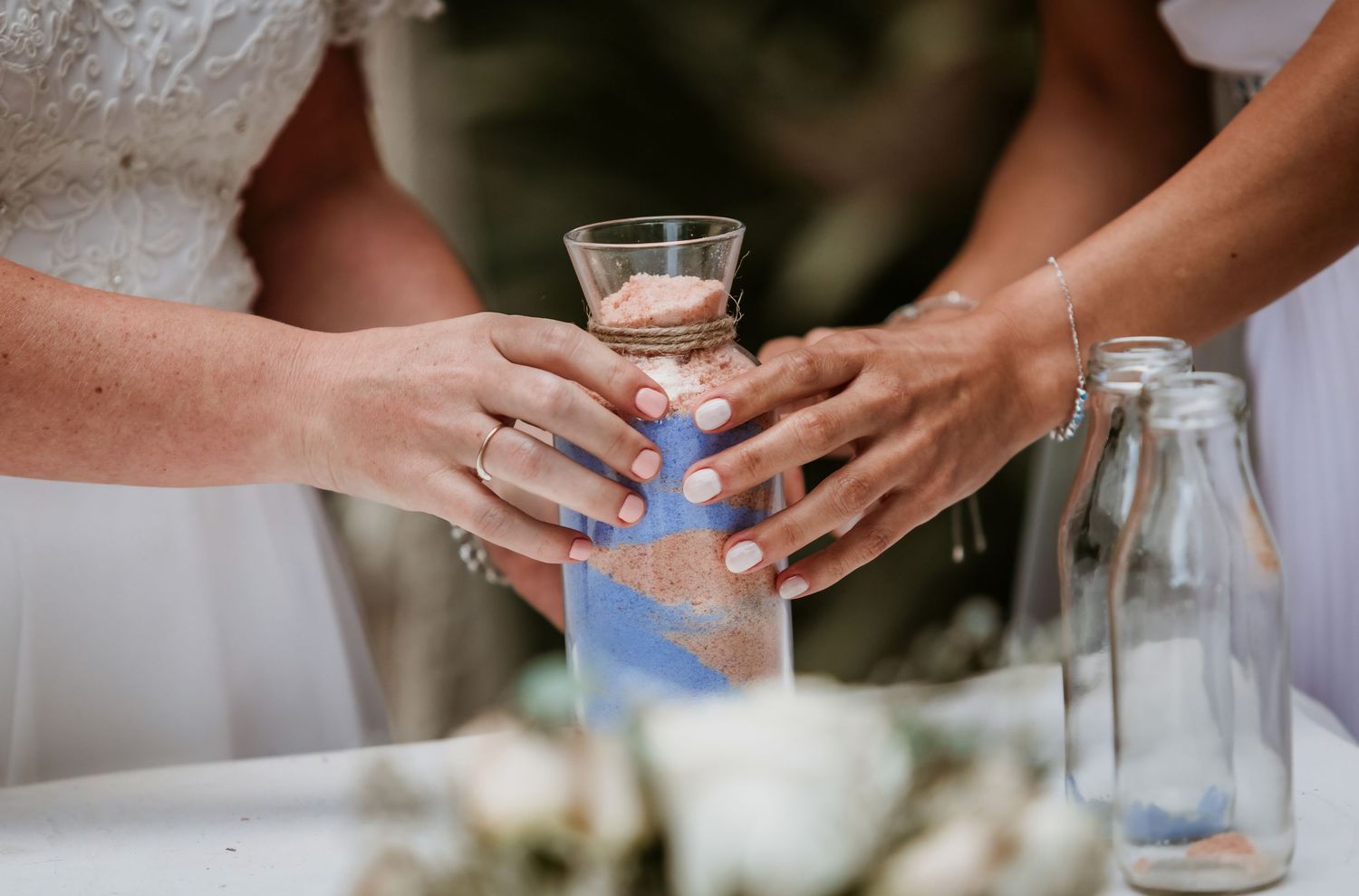 Two brides hold a sand ceremony vase together during their wedding ritual.