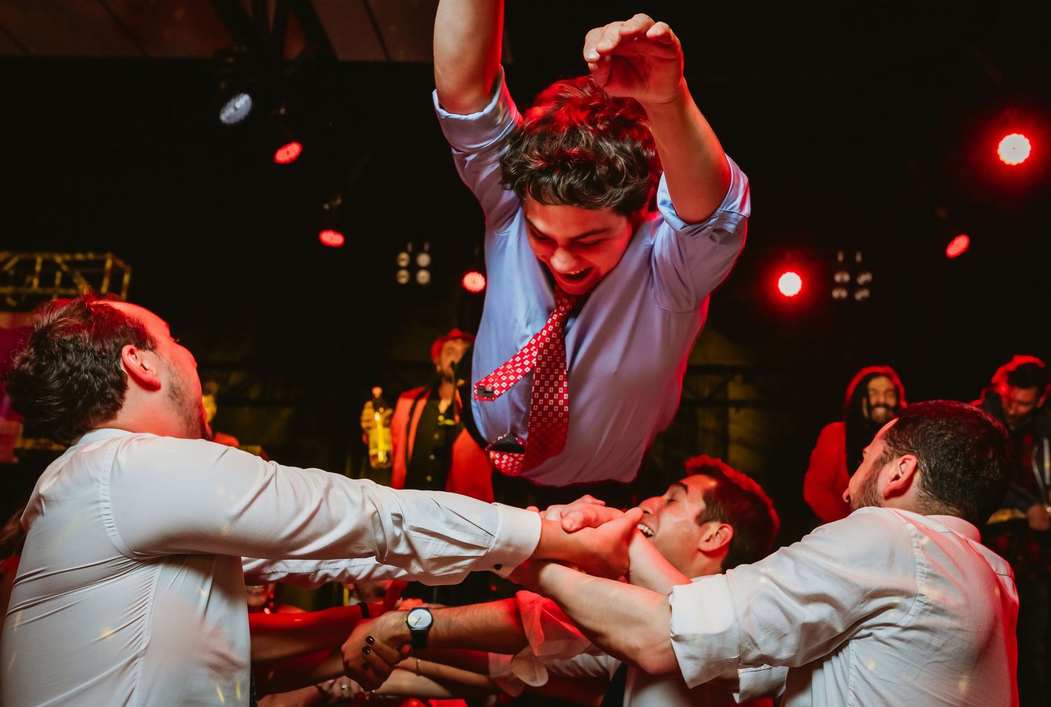 Groom lifted by groomsmen on the dance floor at an energetic wedding celebration.