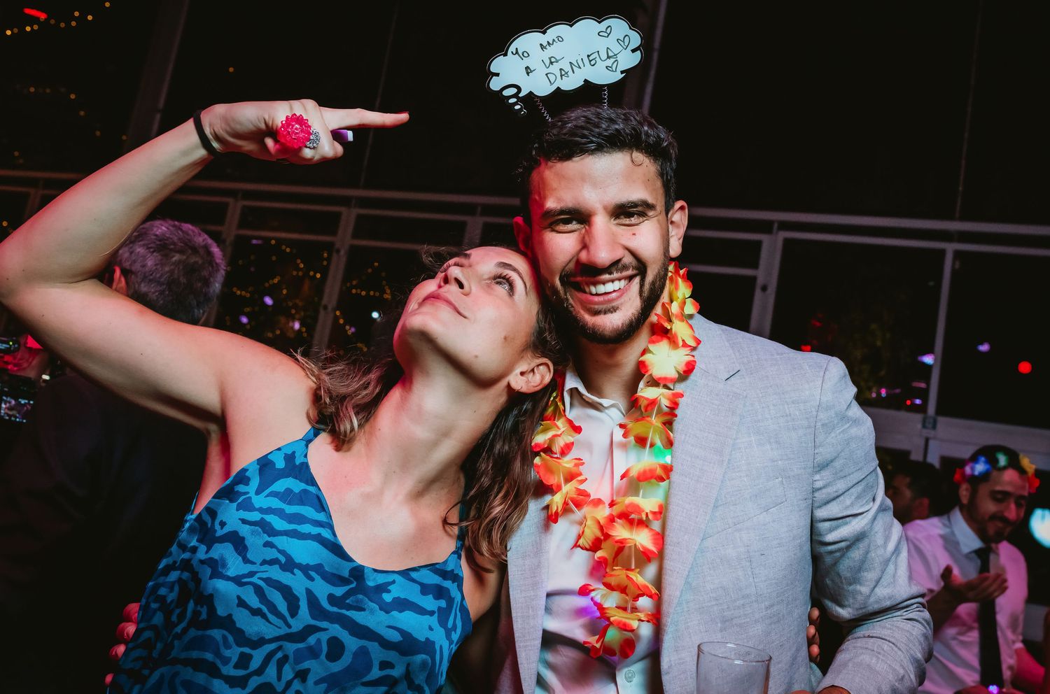 Couple smiling at wedding party, woman in blue dress and man wearing colorful floral lei.