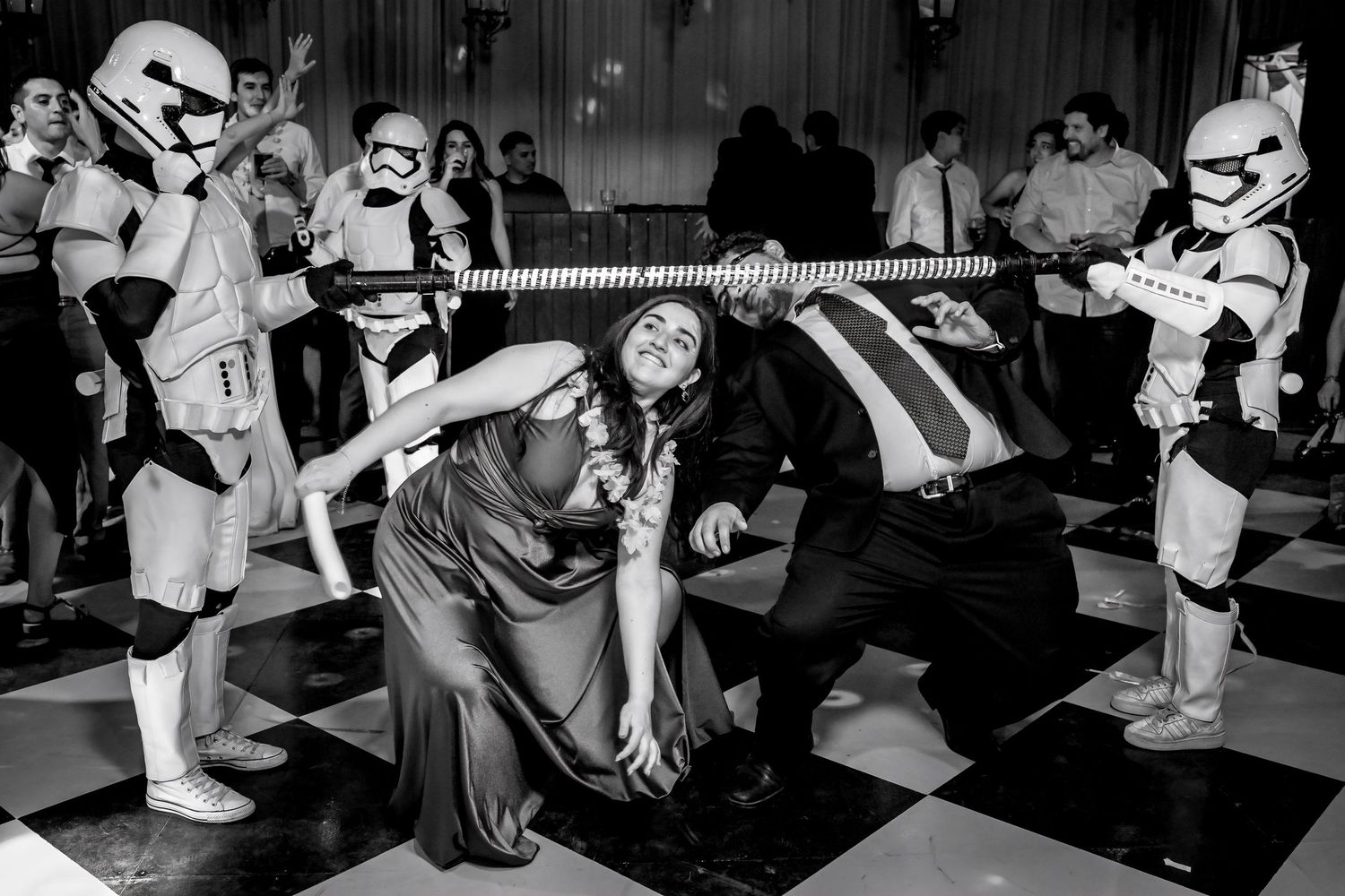 Stormtroopers hold a limbo bar as guests duck under it on a checkered dance floor.