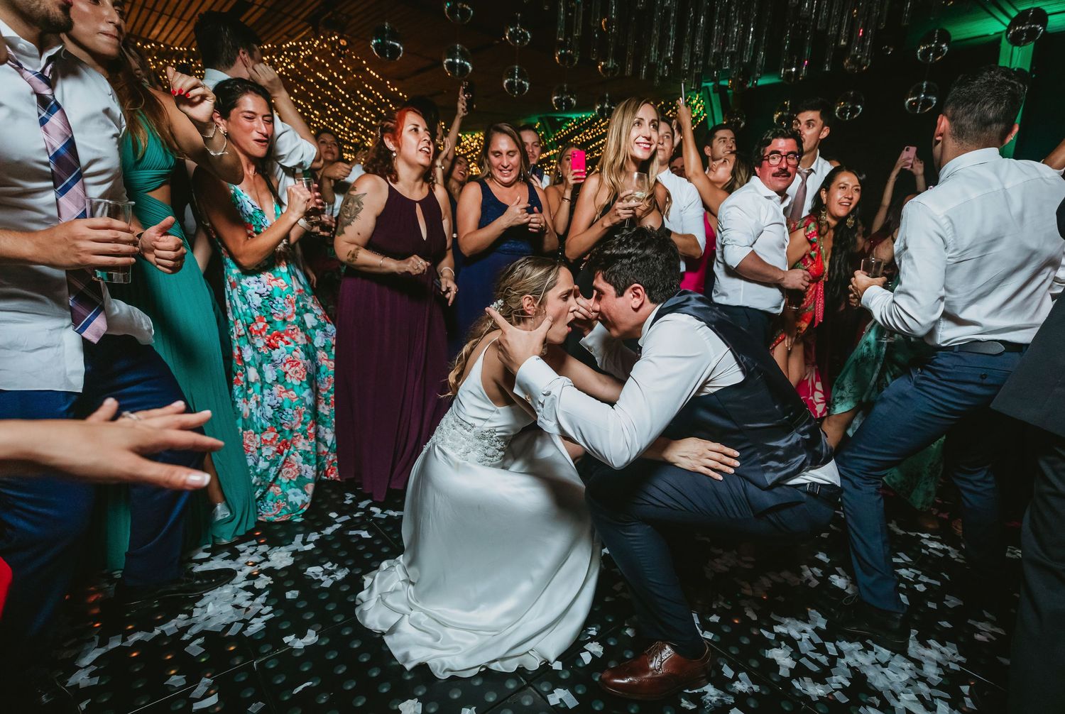A bride and groom share an intimate moment on the dance floor surrounded by joyful guests at their wedding reception.