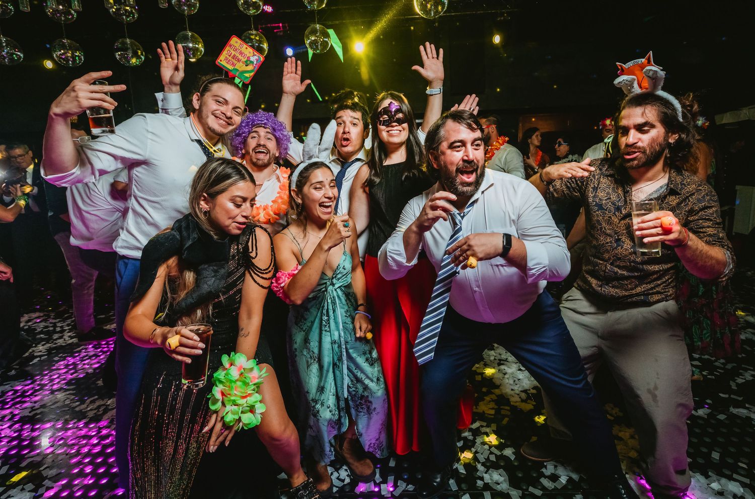 Group of party guests posing and celebrating together at a vibrant nightclub event with confetti.
