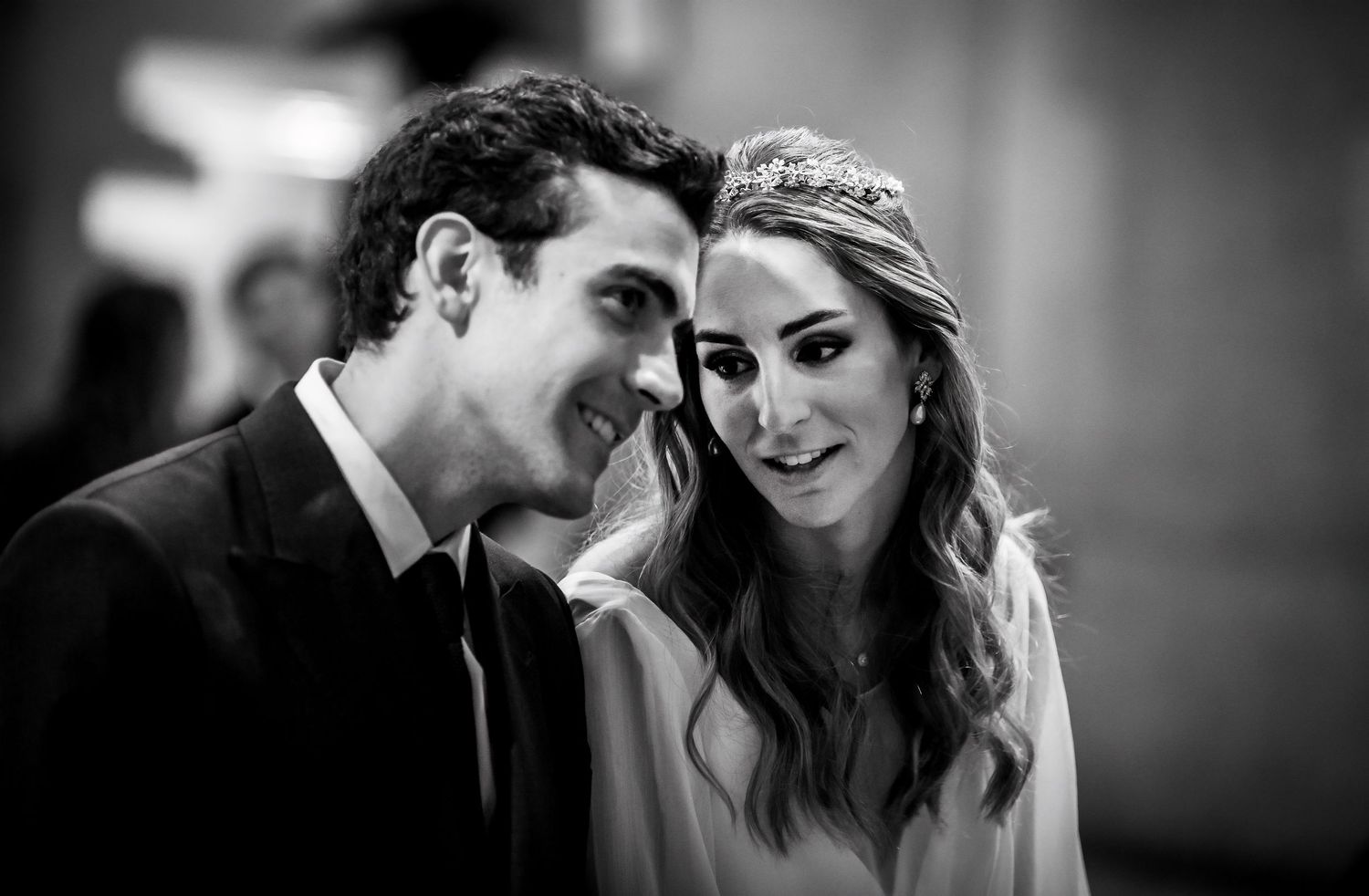 Black and white close-up of smiling bride wearing tiara and groom sharing a tender moment at their wedding.