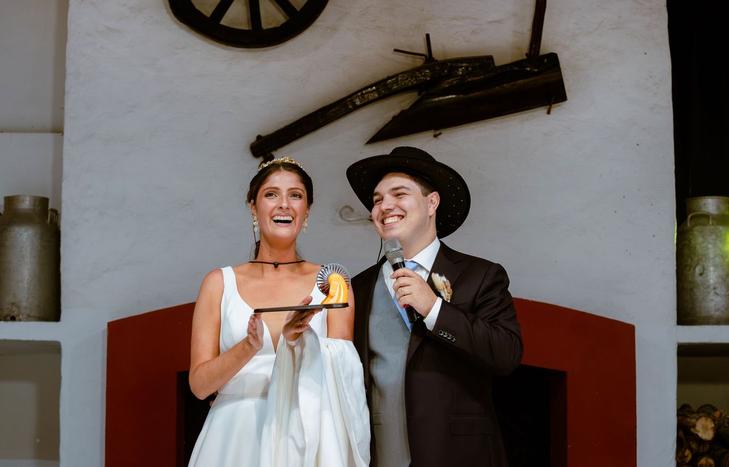 Bride and groom laugh together while holding candles outside rustic wedding venue.