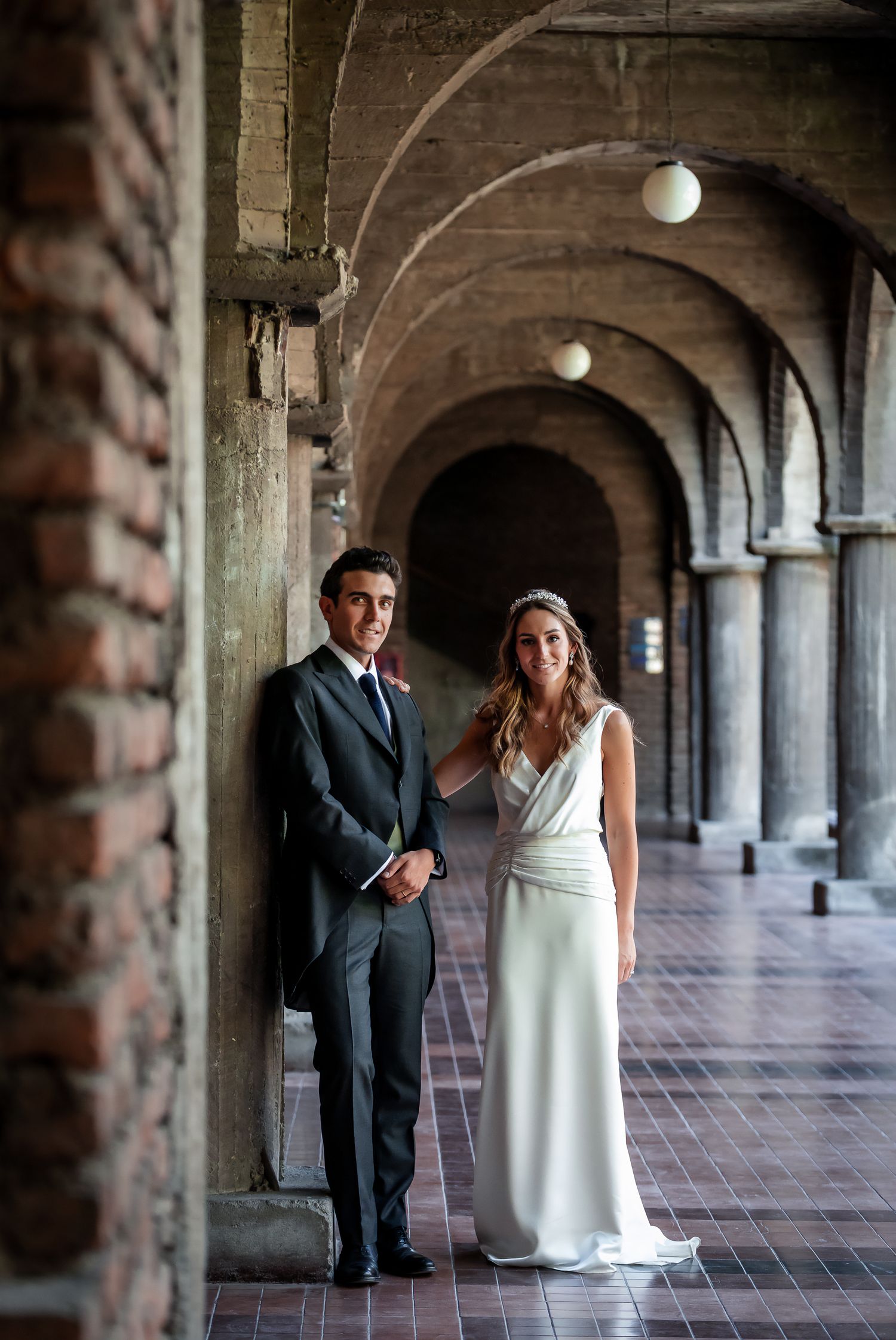 Bride and groom posing in a stunning arched brick hallway with tiled floor on their wedding day.