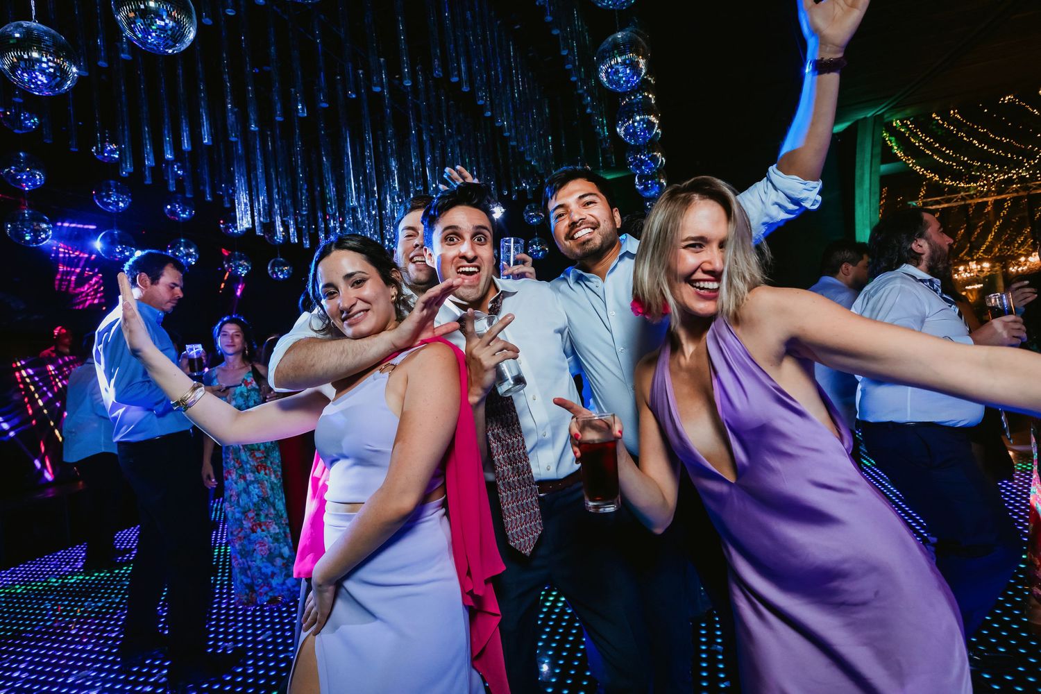 Four wedding guests dancing and posing on colorful disco dance floor.