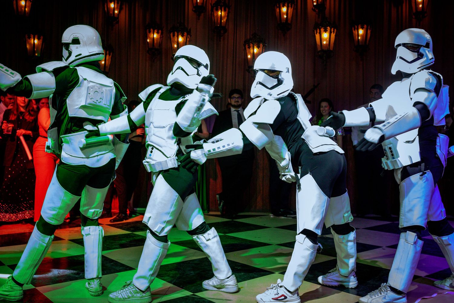 Four Star Wars Stormtroopers dancing in a line under green lights at a wedding reception.