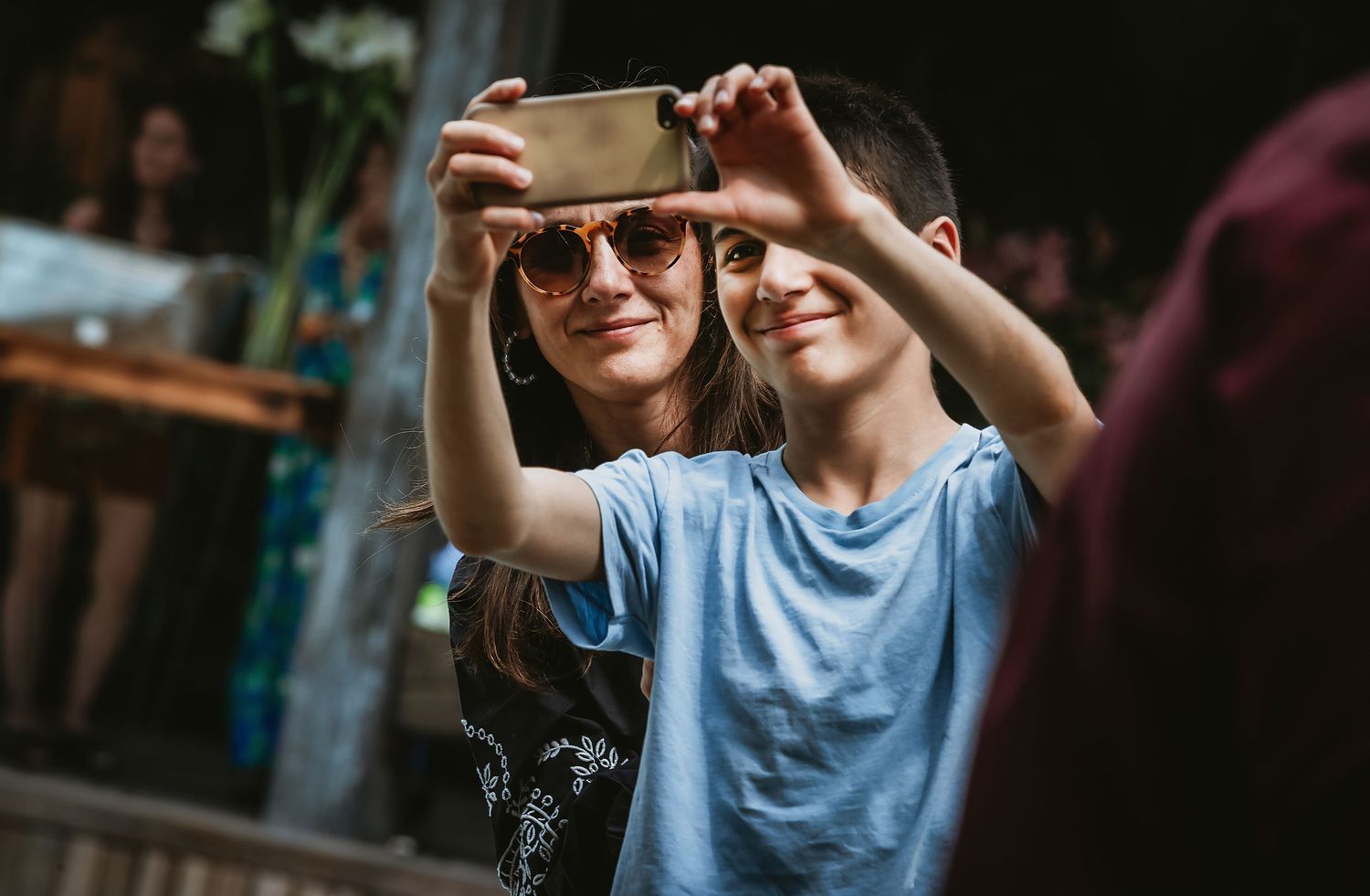 Two friends taking a selfie together outdoors, smiling, with one wearing sunglasses and holding a smartphone.