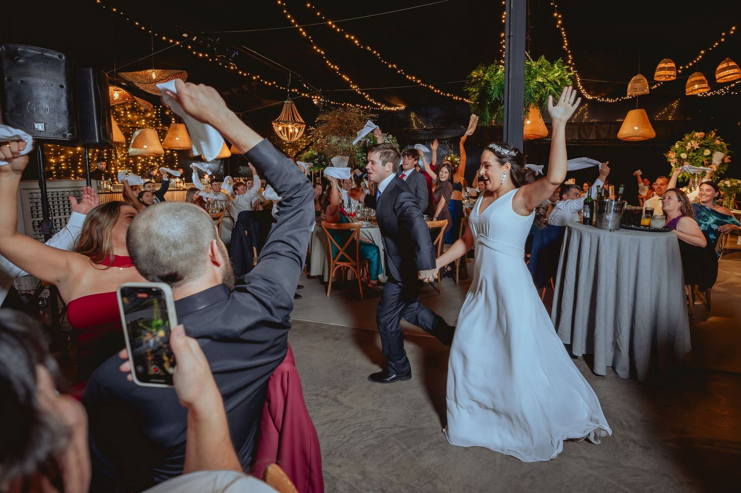 Bride and groom make a grand entrance as excited wedding guests celebrate around them.