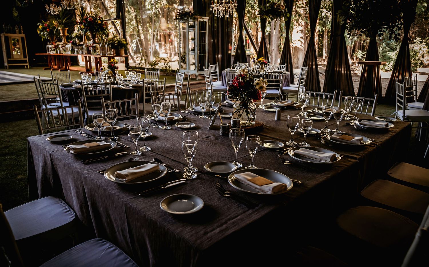 Formal wedding reception table set with crystal glassware, silver charger plates, and floral centerpiece on dark linen.