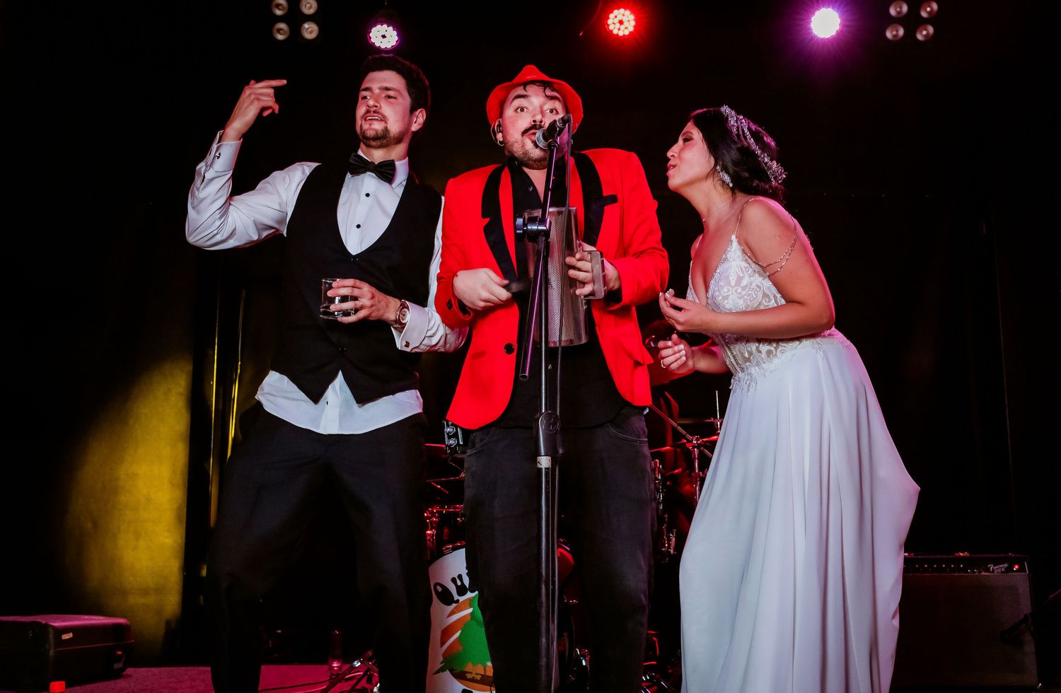 Groom and bride singing on stage with live band performer at wedding reception.