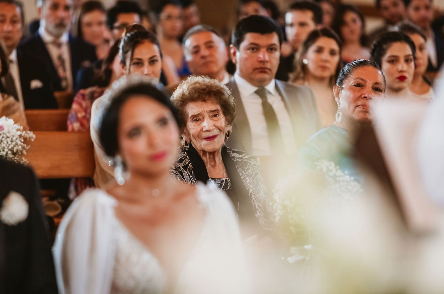 Elderly woman smiling warmly while watching bride during emotional wedding ceremony in church.