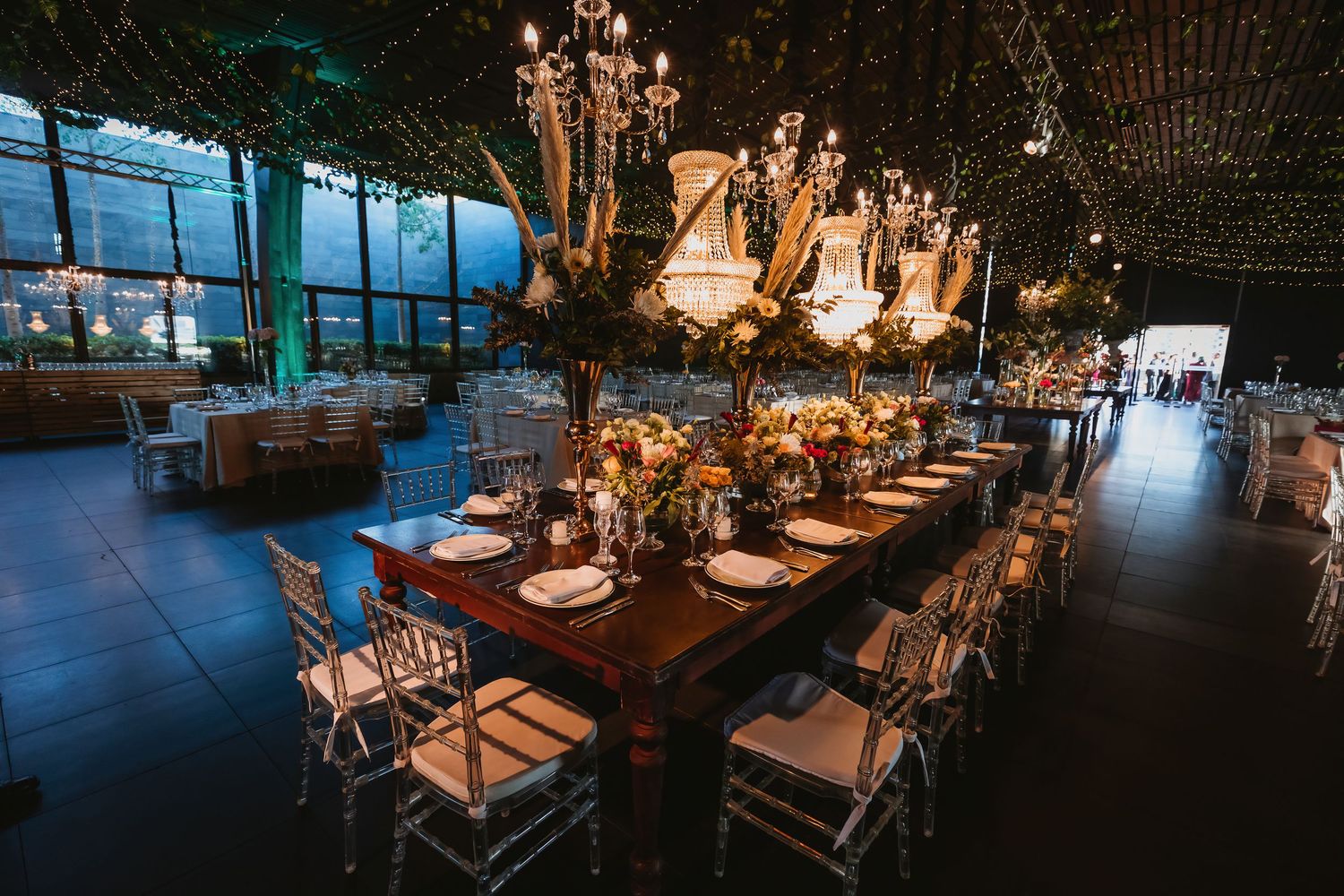 Luxurious wedding reception hall with long wooden tables, crystal chandeliers and floral centerpieces.