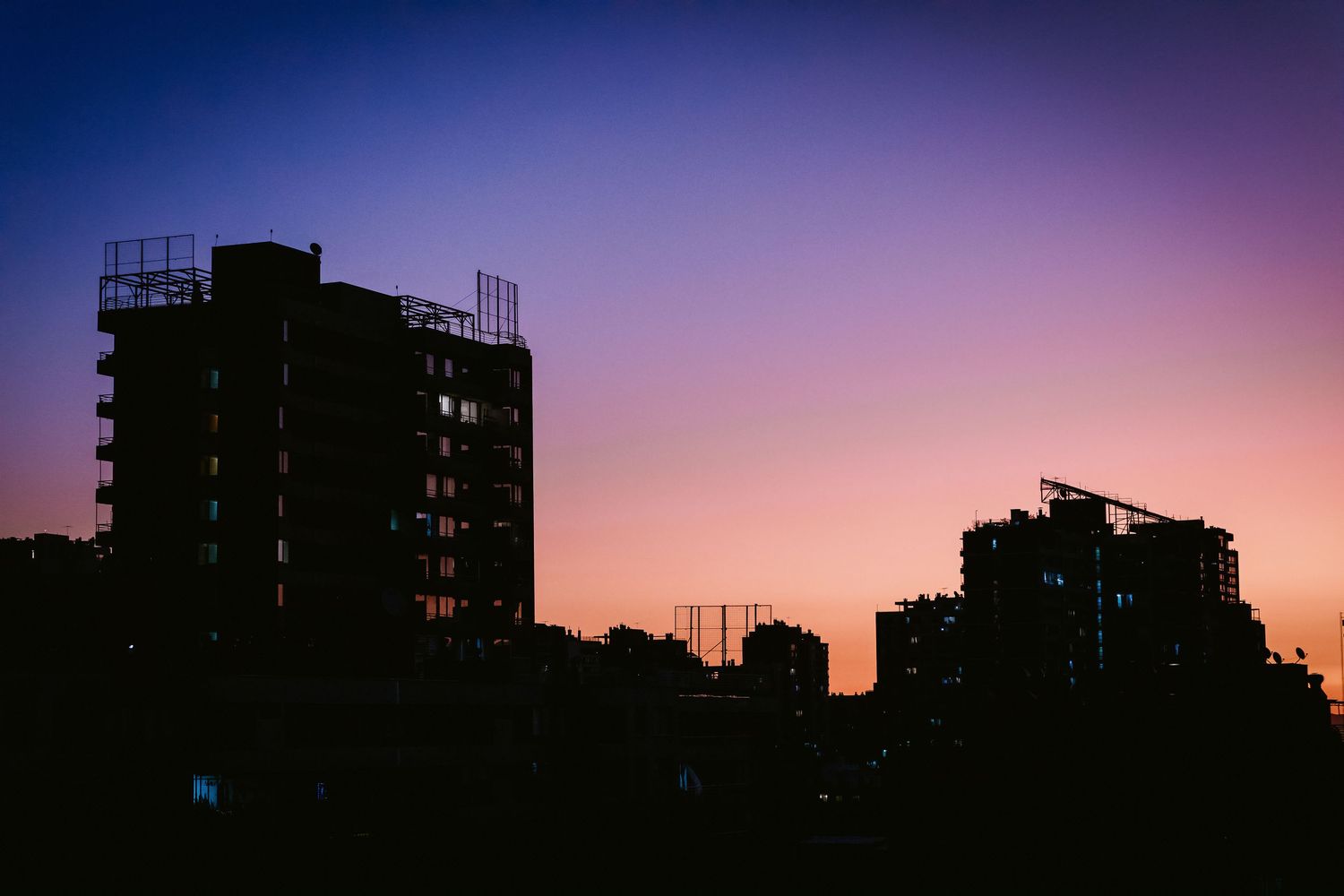 City buildings silhouetted against a stunning purple and orange sunset sky.
