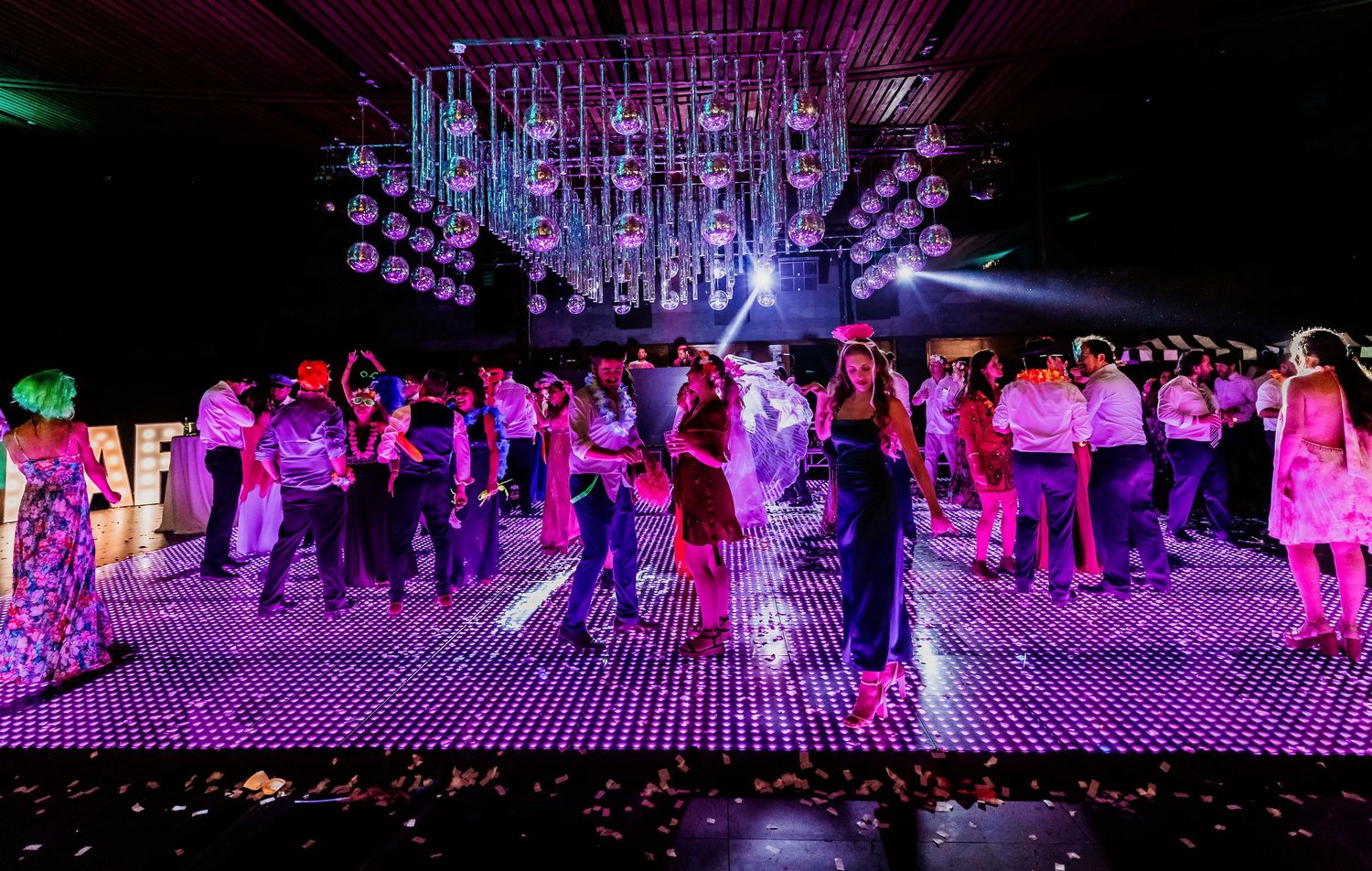 Elegant wedding reception with guests dancing on a large illuminated purple dance floor at night.