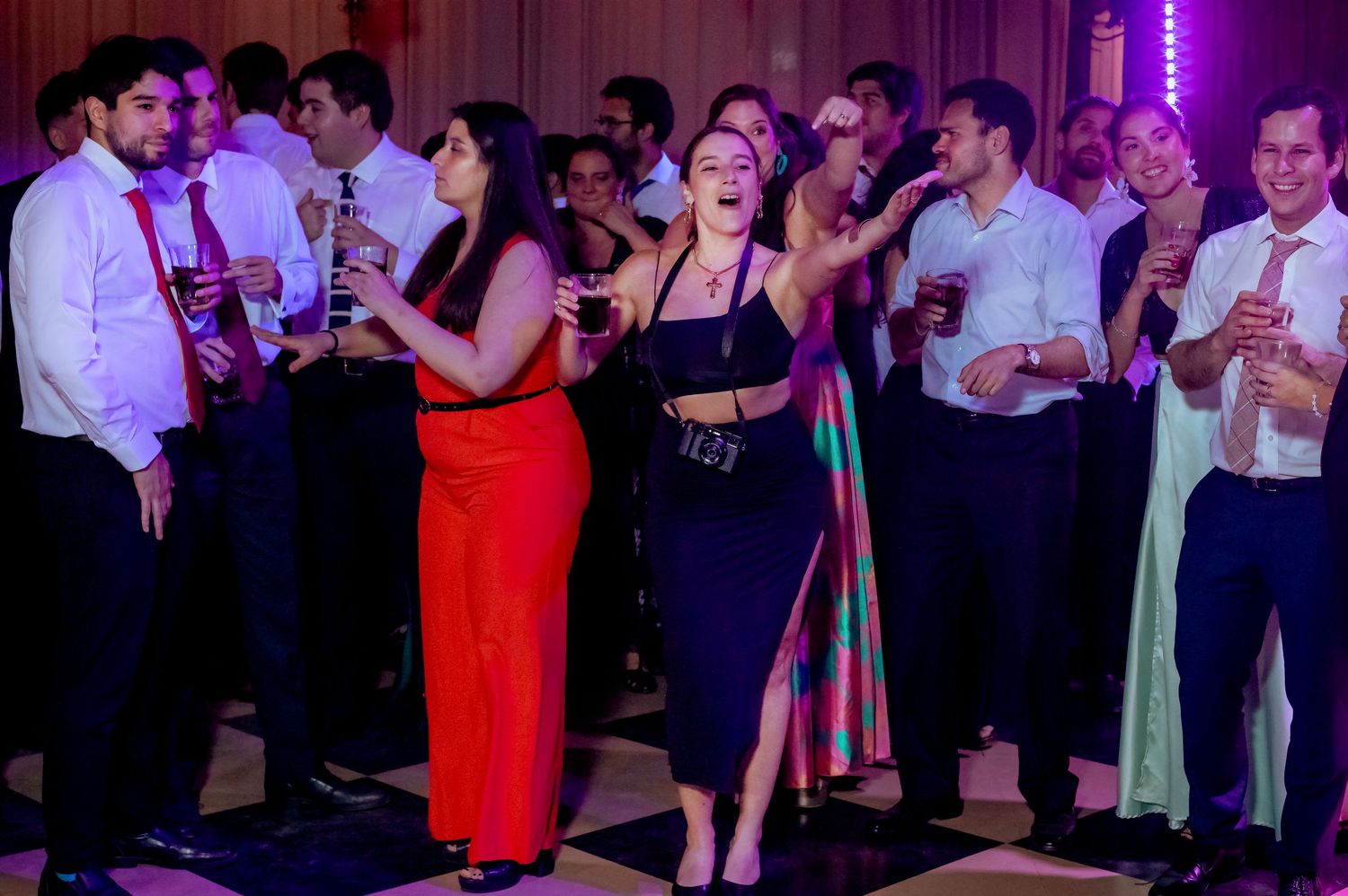 Guests singing and celebrating with drinks at lively wedding reception on classic black and white dance floor.
