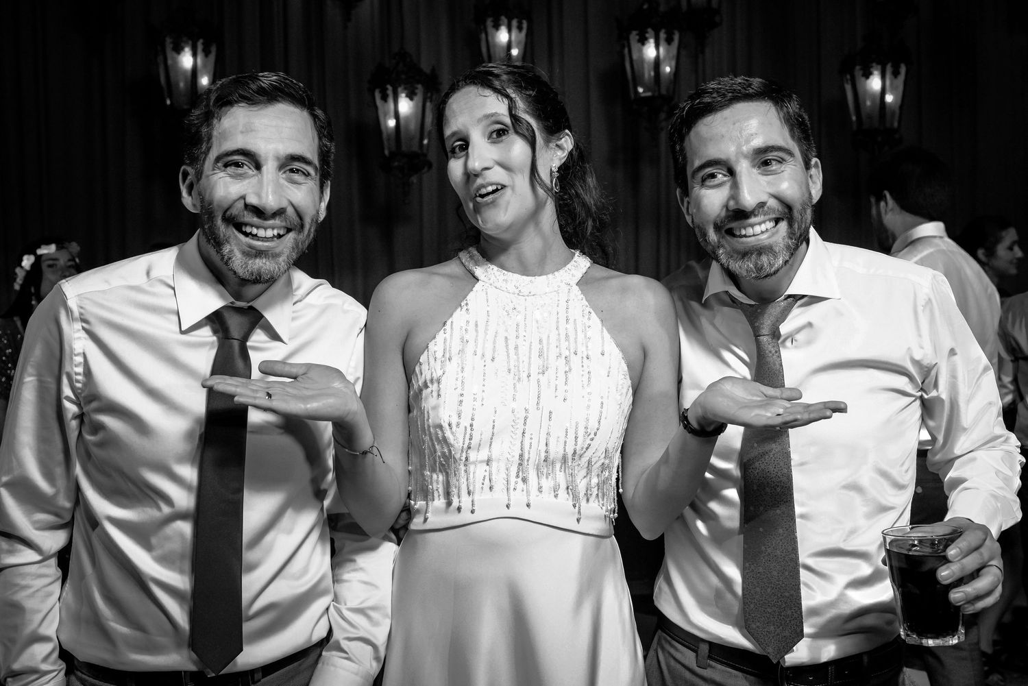 Bride poses with two groomsmen in black and white wedding reception photo.