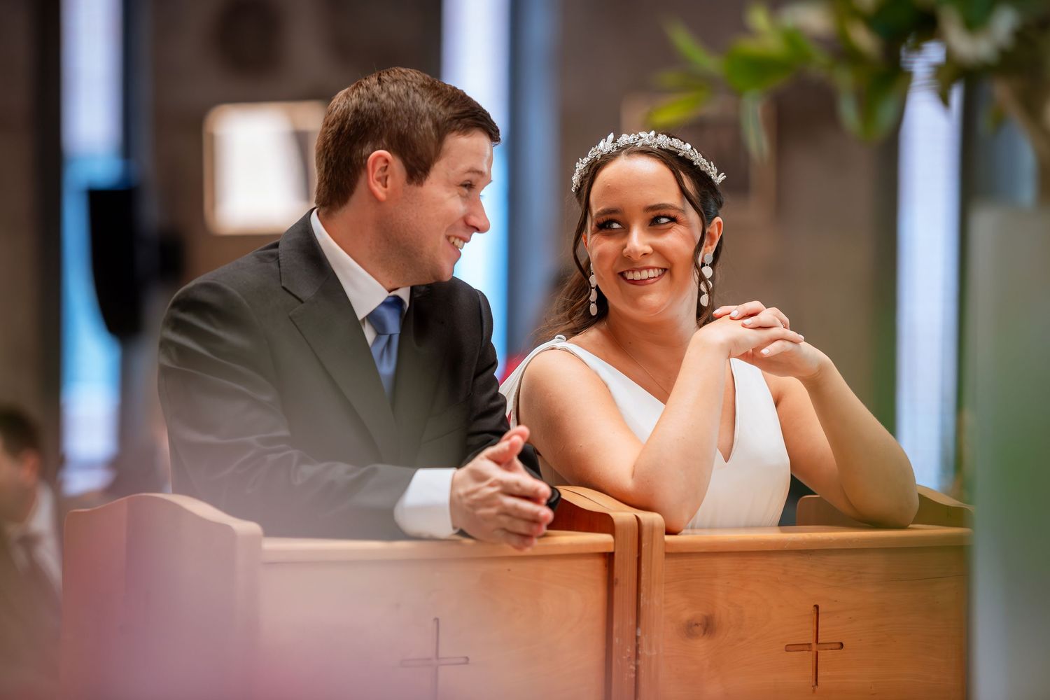 Smiling bride in tiara and groom share a tender moment together during their church wedding.